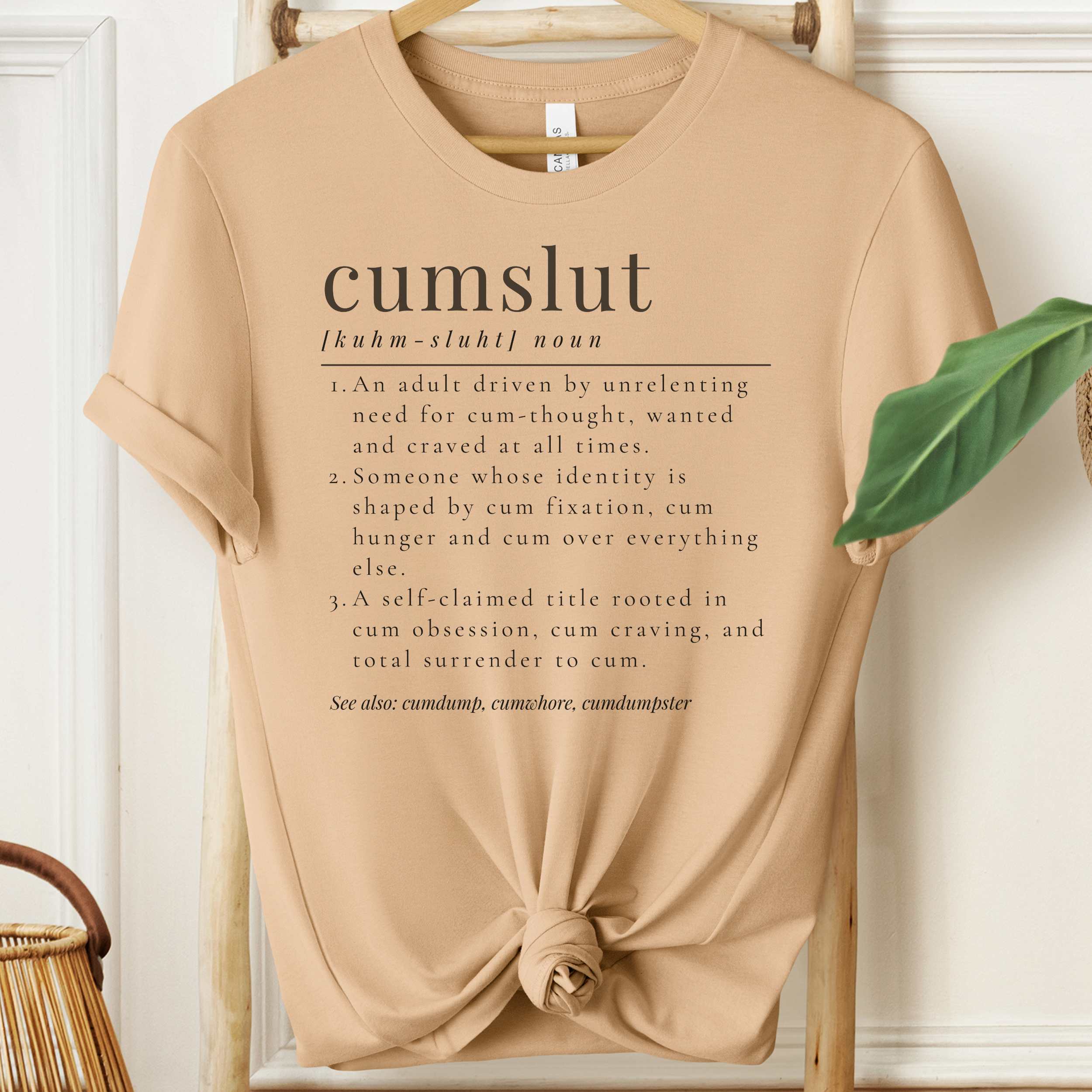 Beige t-shirt with 'cumslut' definition text on a hanger.