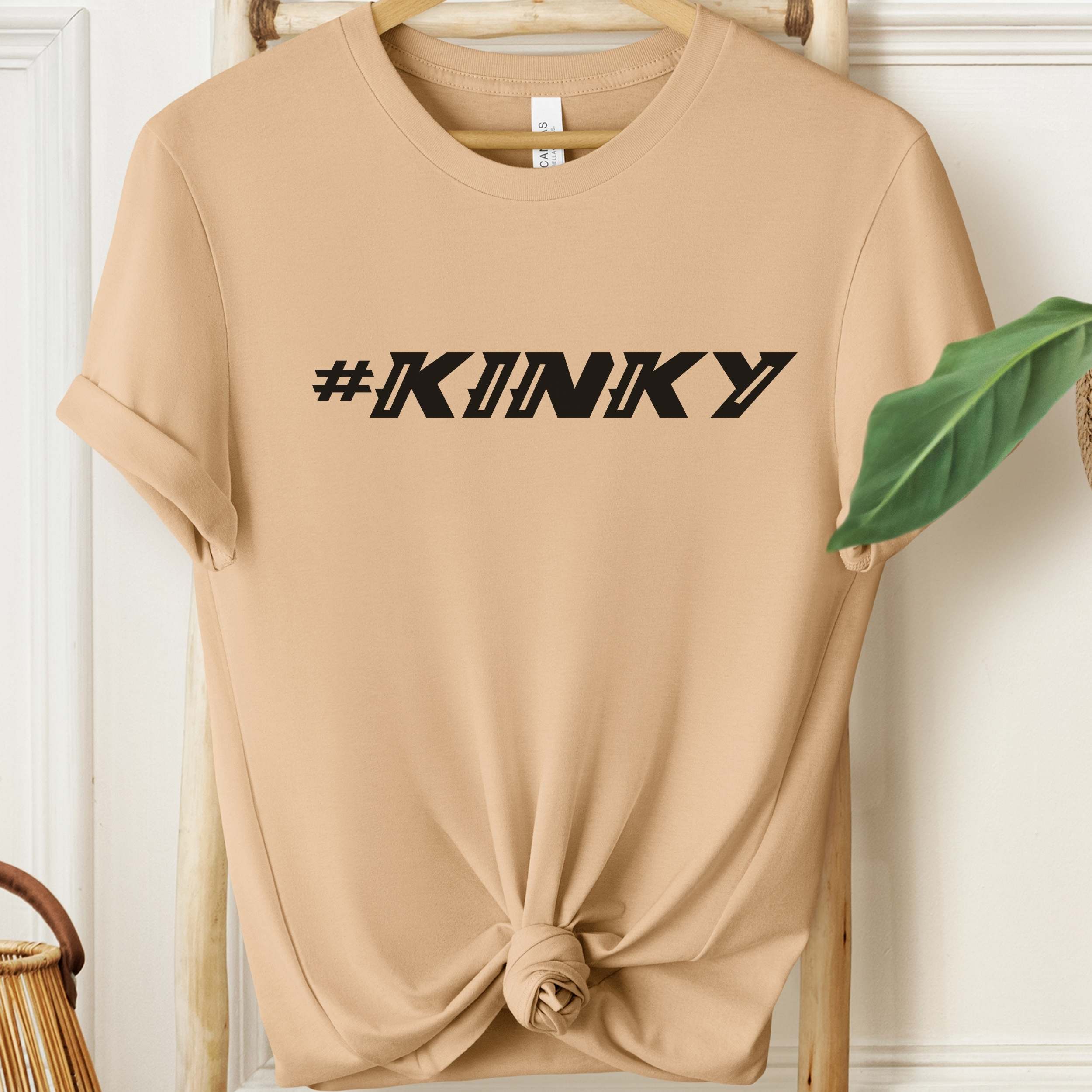Beige t-shirt with '#KINKY' text on a wooden hanger.