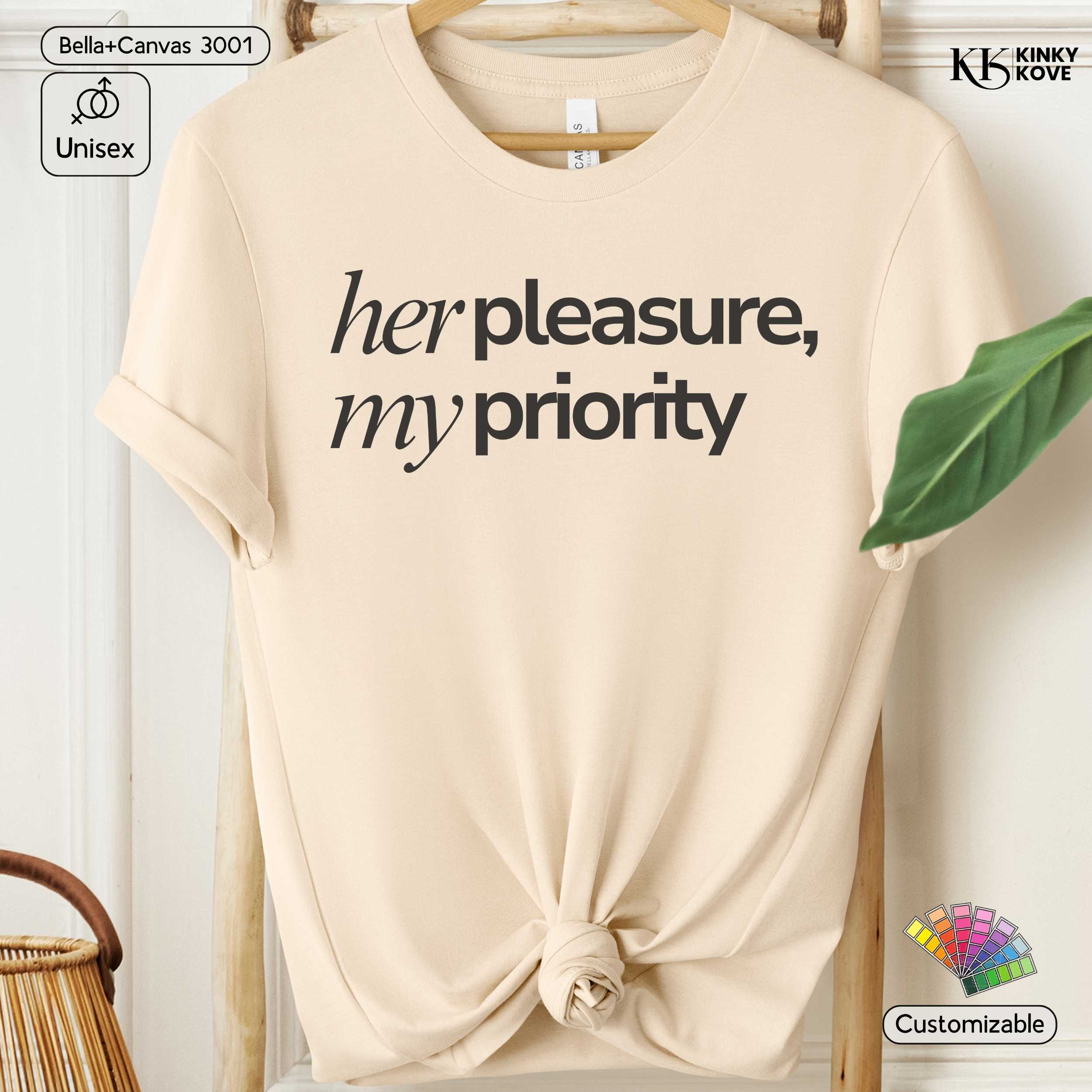 Beige t-shirt with 'her pleasure, my priority' text on a hanger with a plant in the background.