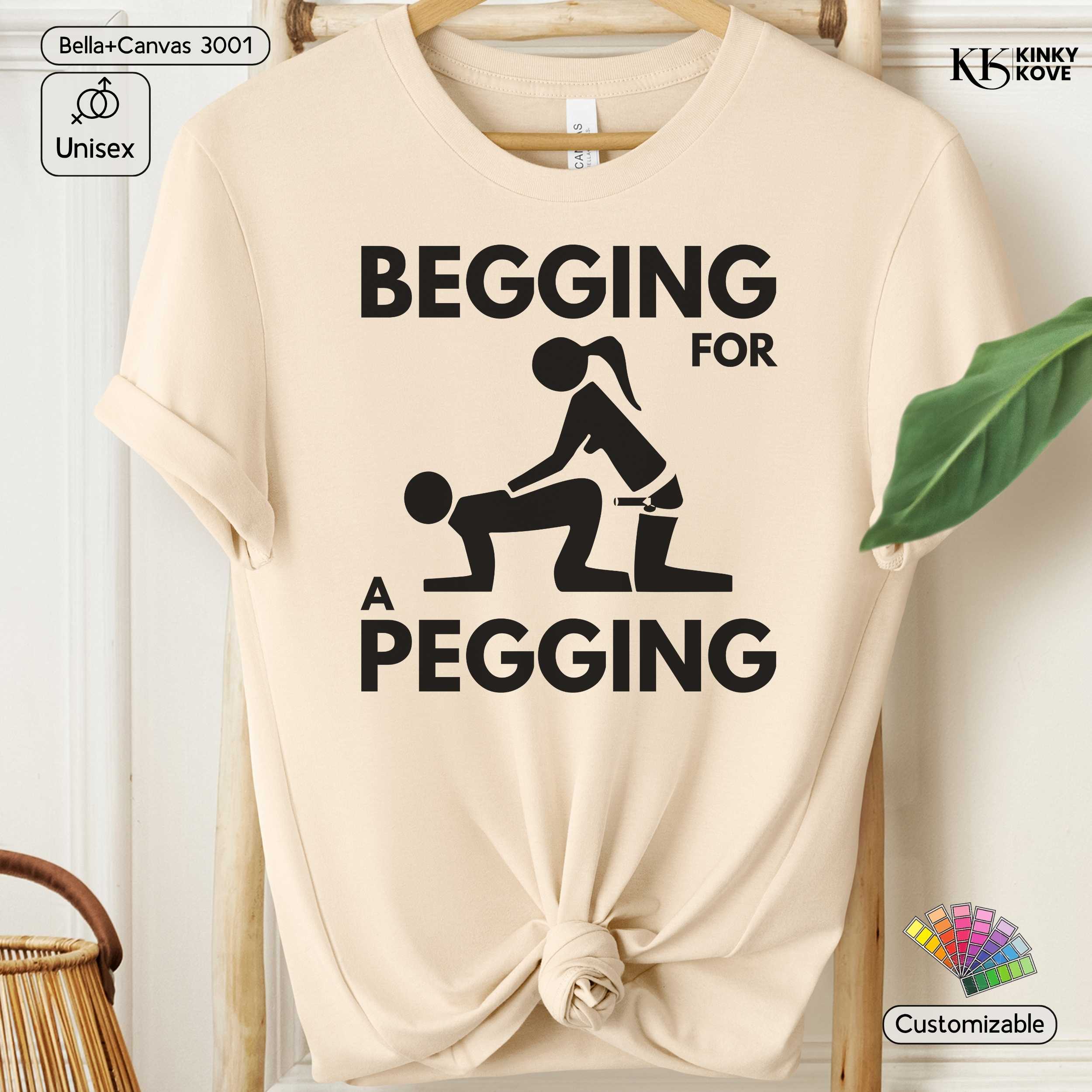 Beige t-shirt with graphic design and text 'Begging for a Pegging' on a hanger.