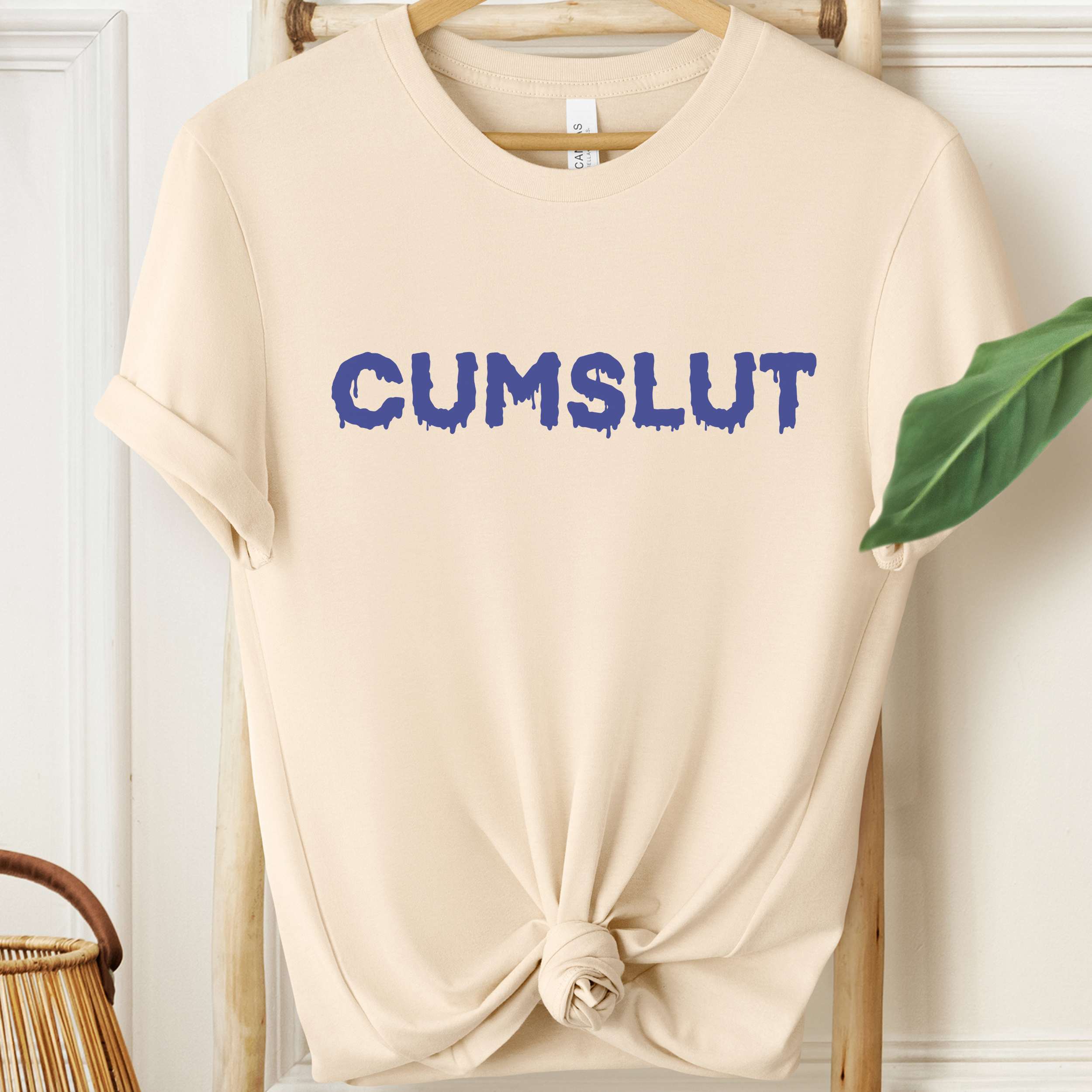 Beige t-shirt with 'CUMSLUT' printed in blue on a hanger.