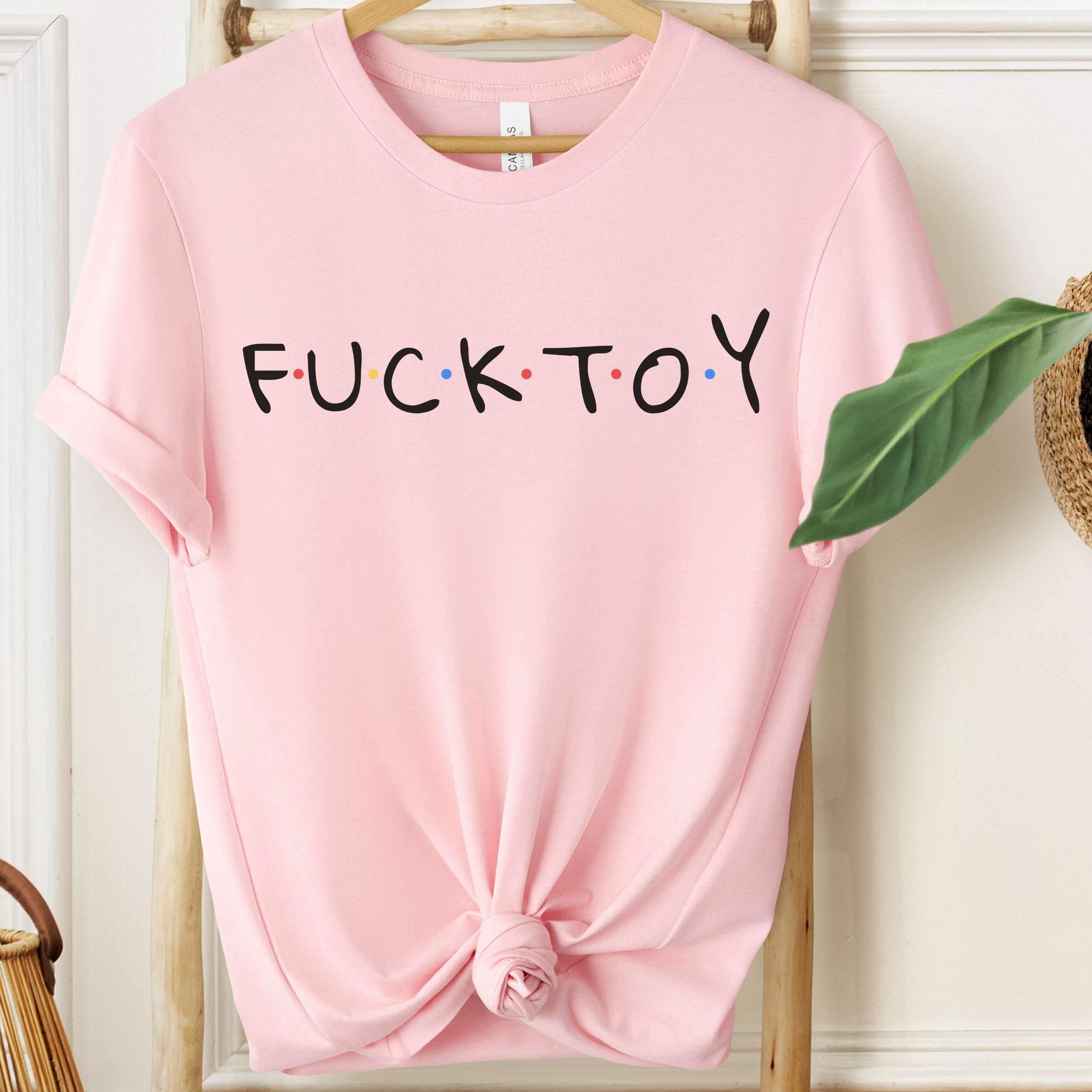Pink t-shirt with text on a wooden hanger against a white wall.