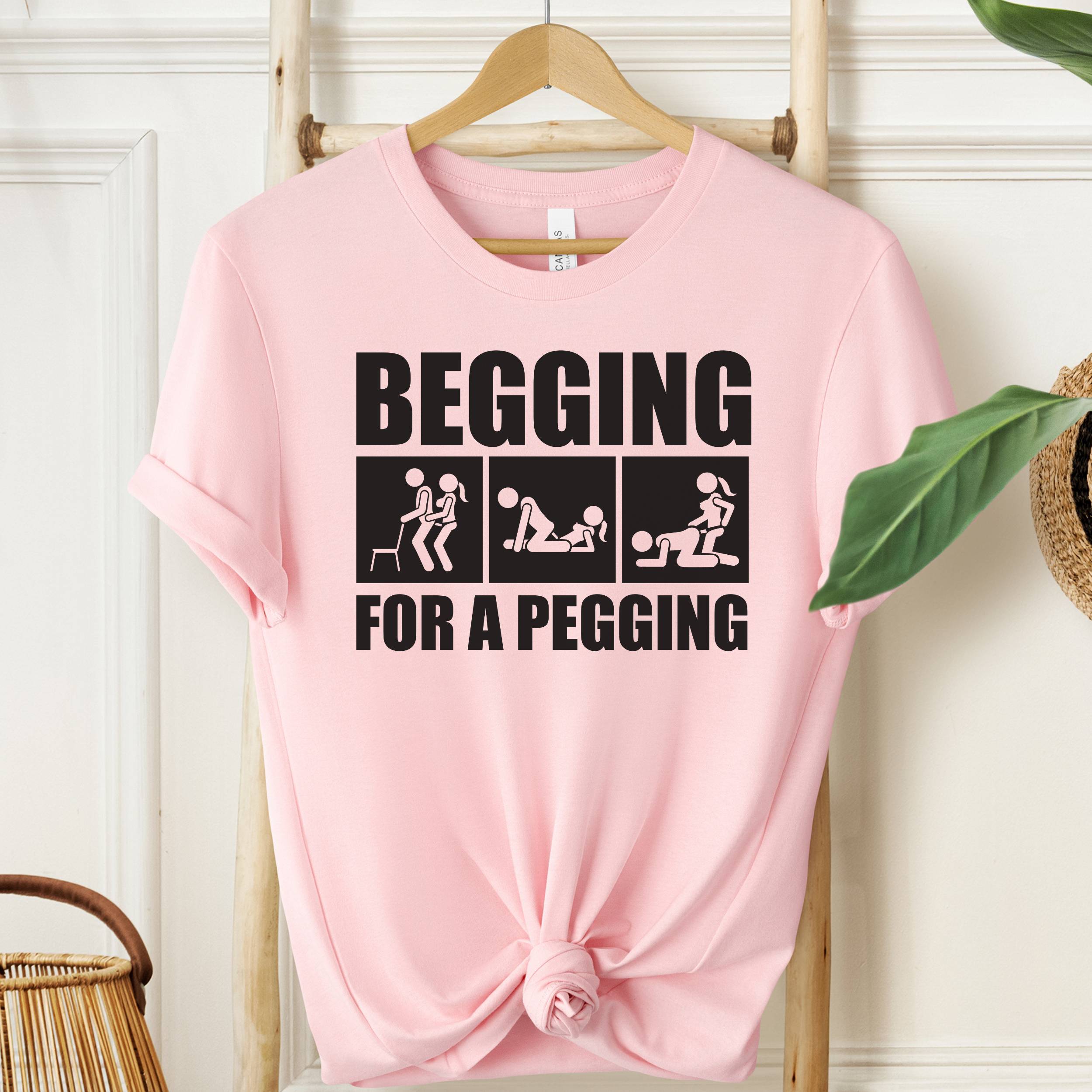 Pink t-shirt with graphic text on a hanger against a white wall.