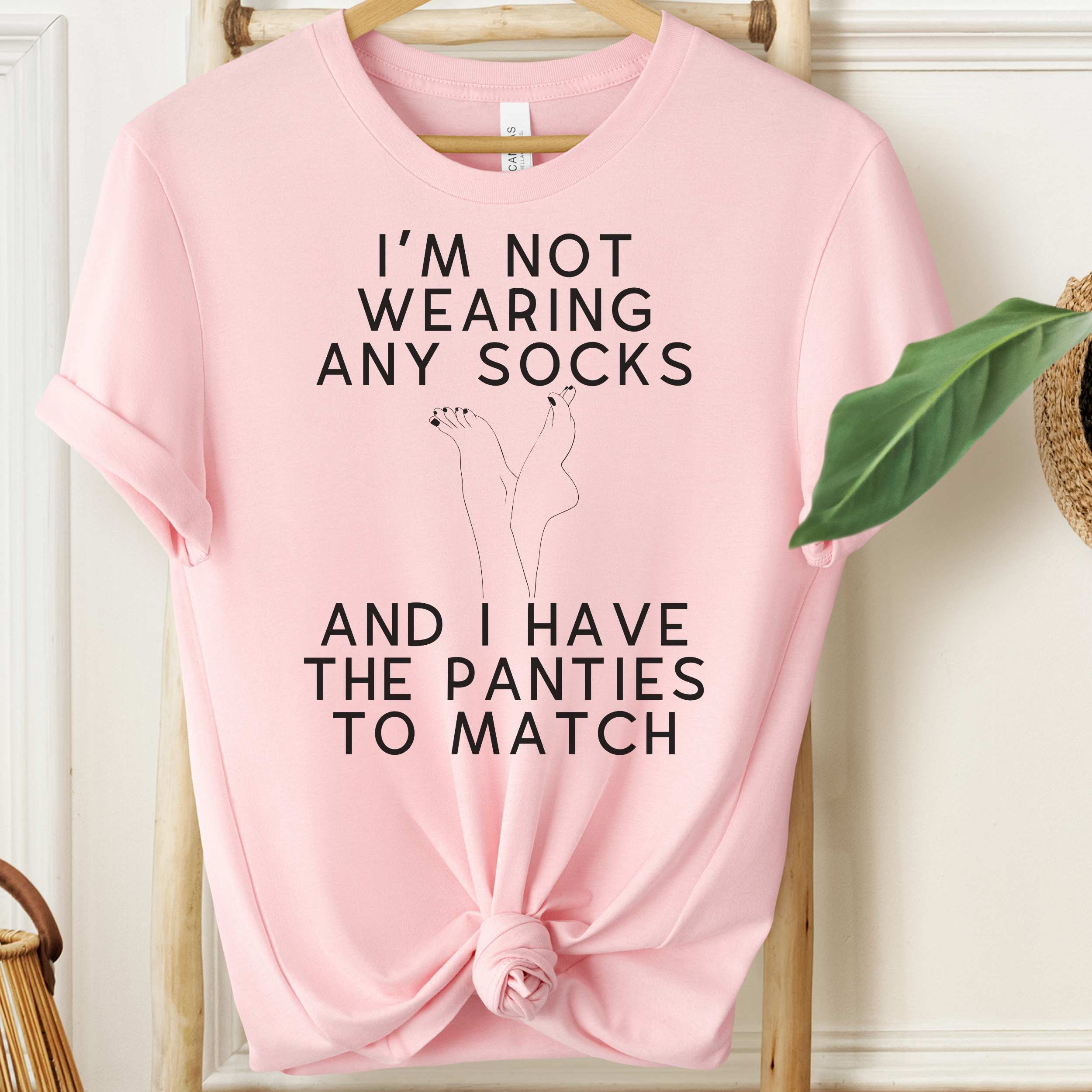 Pink t-shirt with humorous text design on a wooden hanger.
