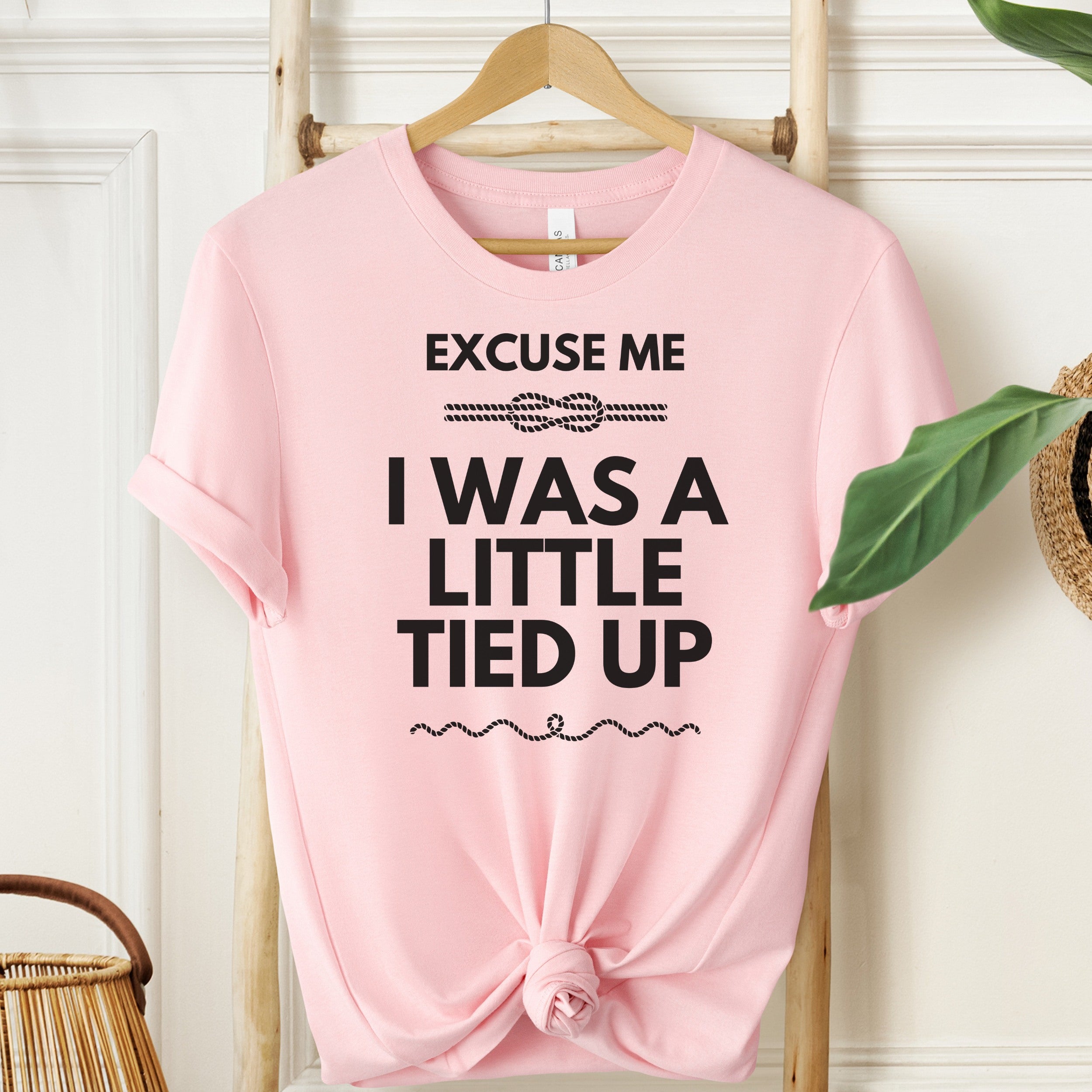 Pink t-shirt with text on a hanger against a white wall.