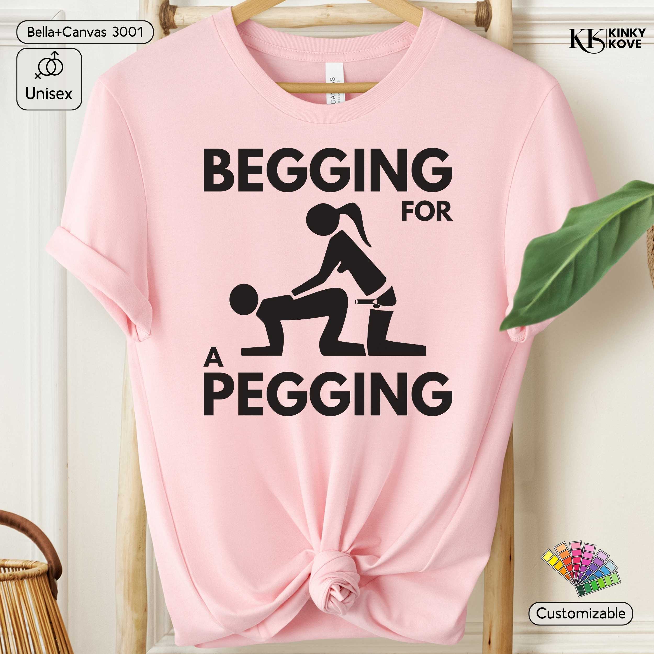Pink t-shirt with graphic design and text 'Begging for a Pegging' on a hanger.
