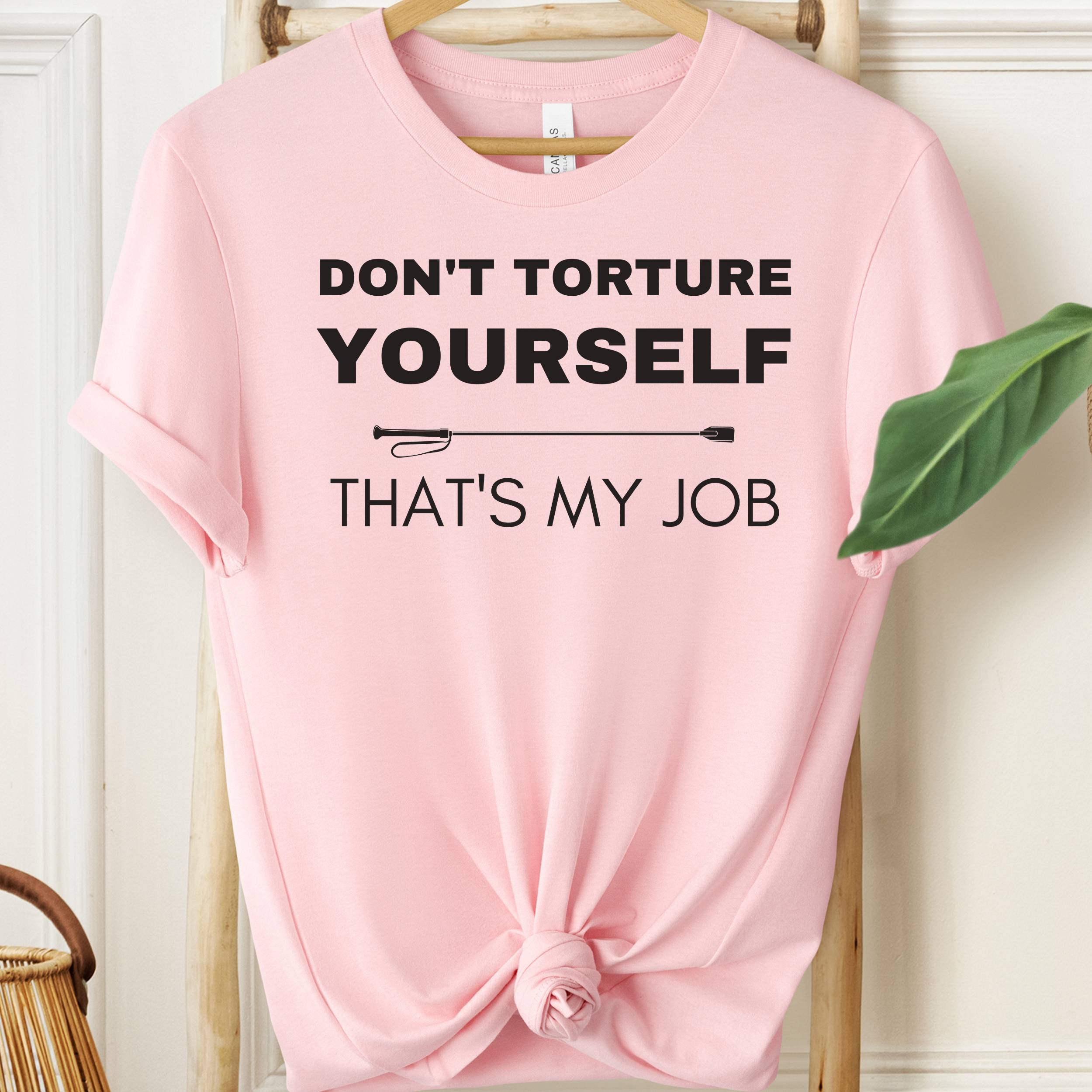 Pink t-shirt with text 'Don't torture yourself, that's my job' on a hanger.