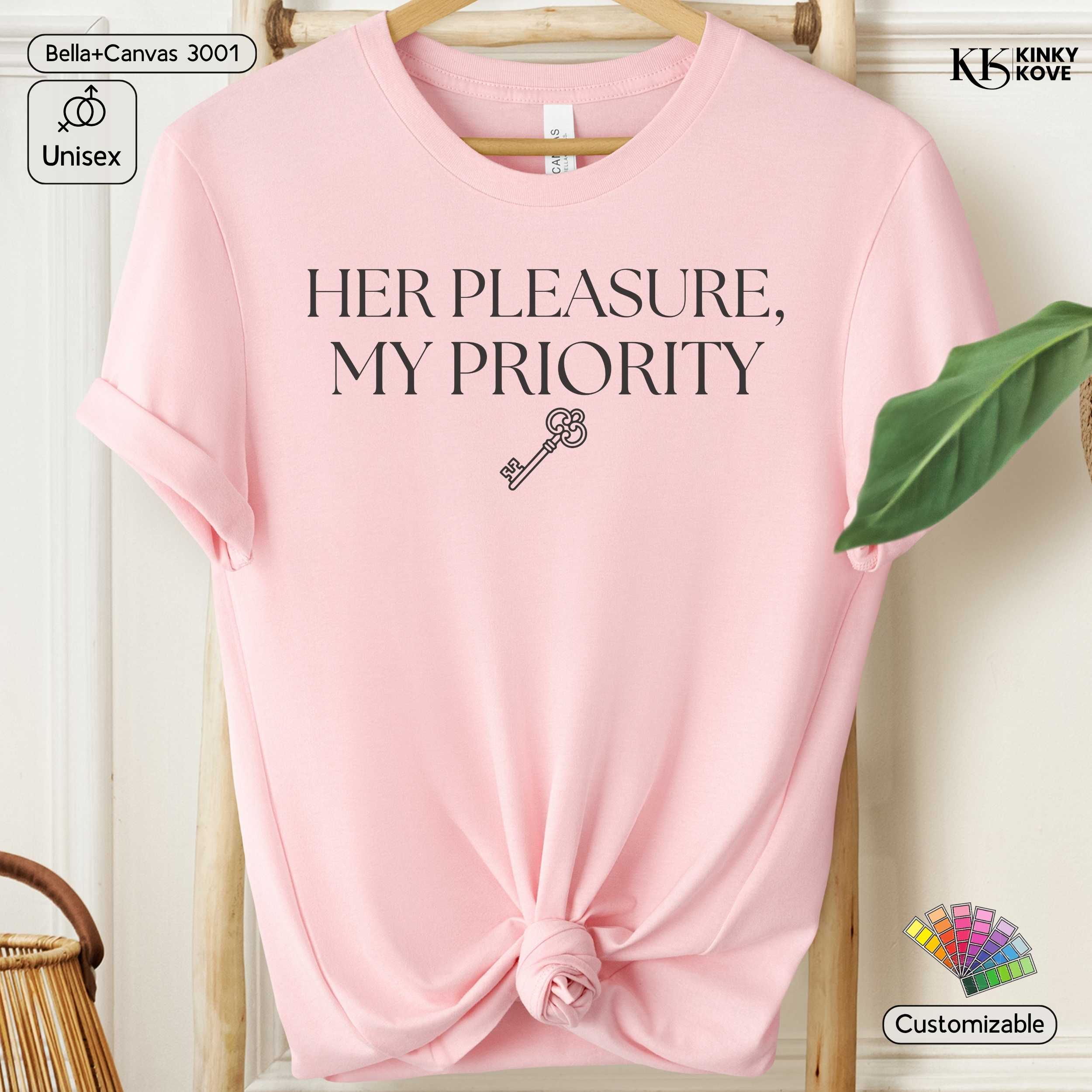 Pink t-shirt with 'HER PLEASURE, MY PRIORITY' text and key graphic on a hanger.
