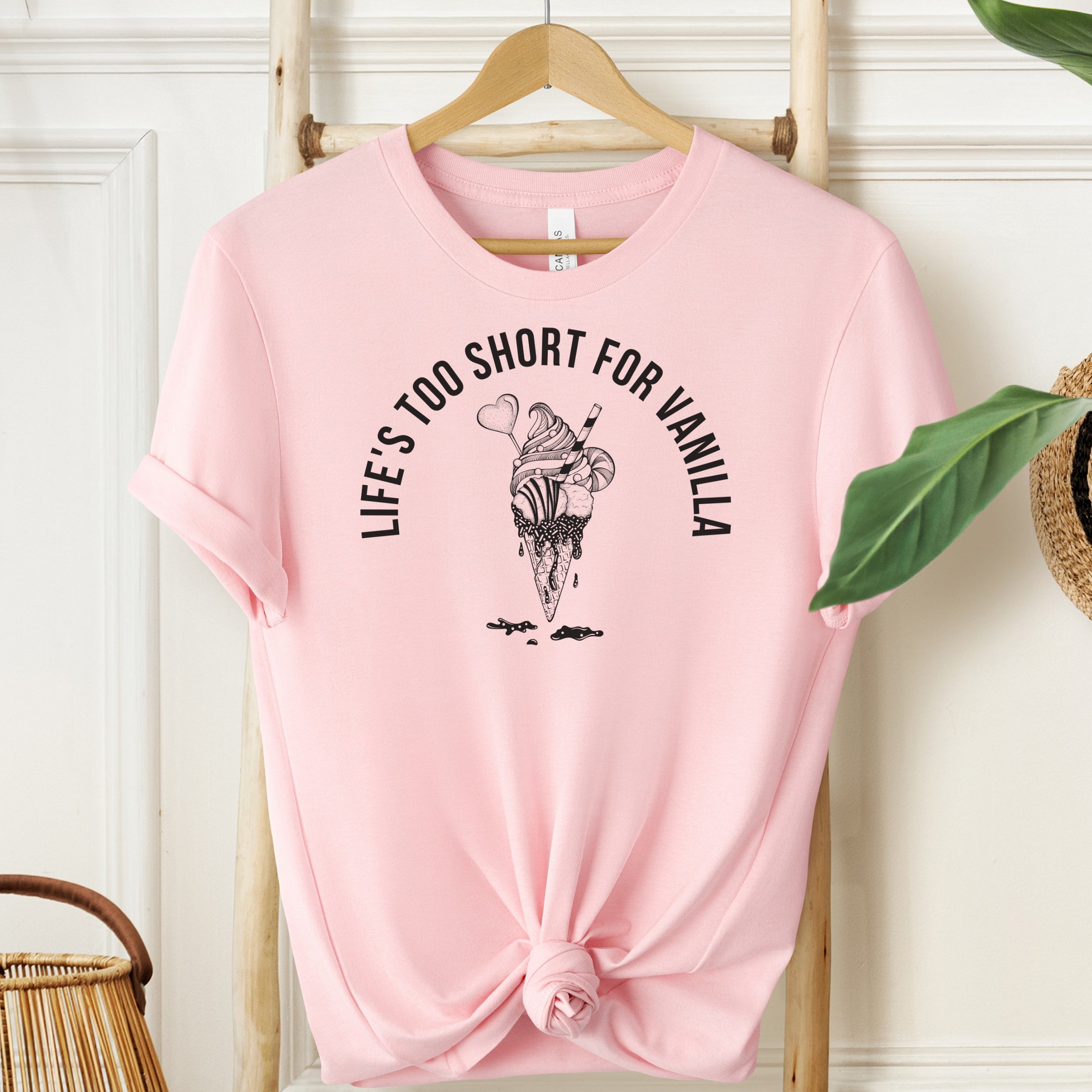 Pink t-shirt with ice cream graphic and text on a hanger against a white wall.