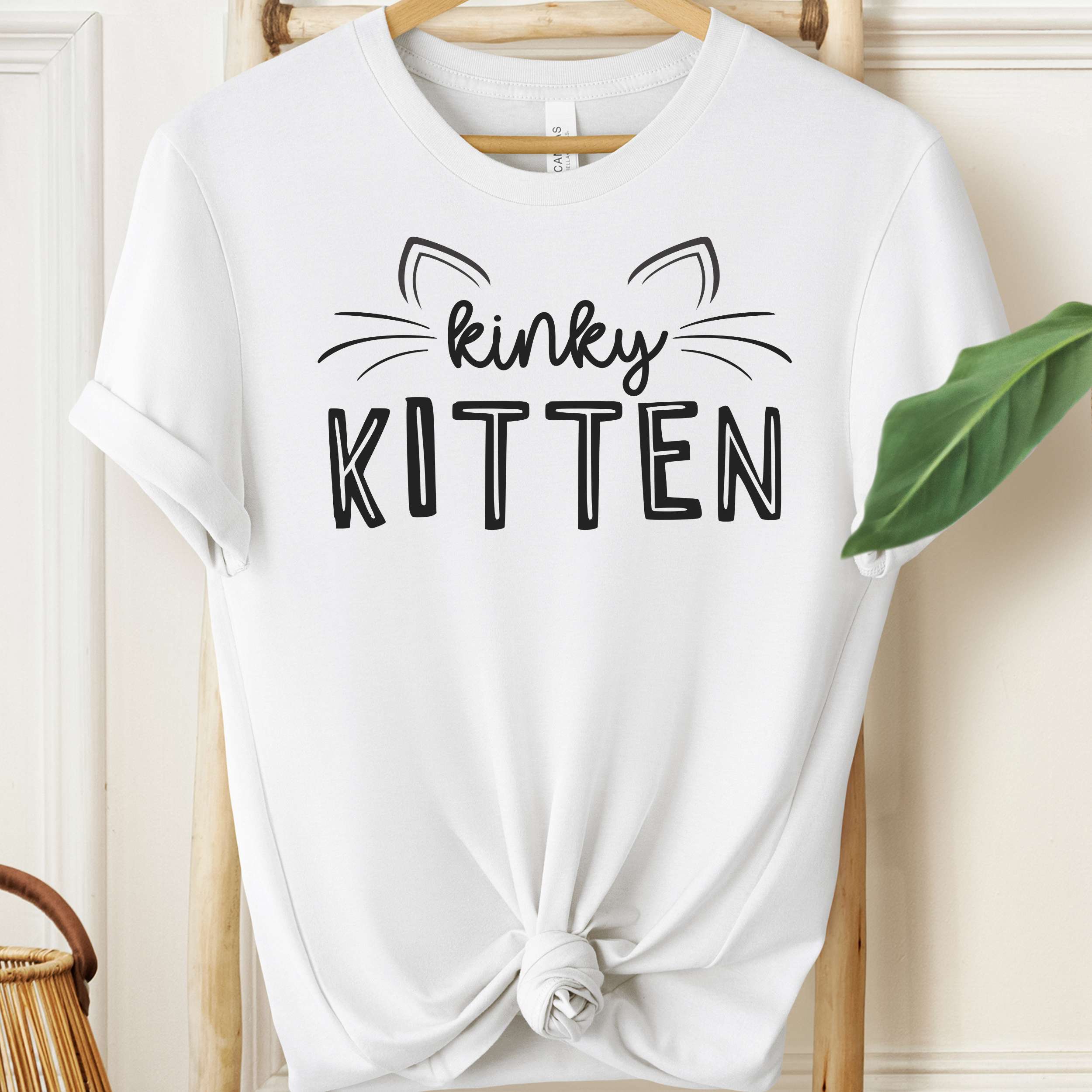 White t-shirt with 'kinky KITTEN' text on a hanger against a neutral background