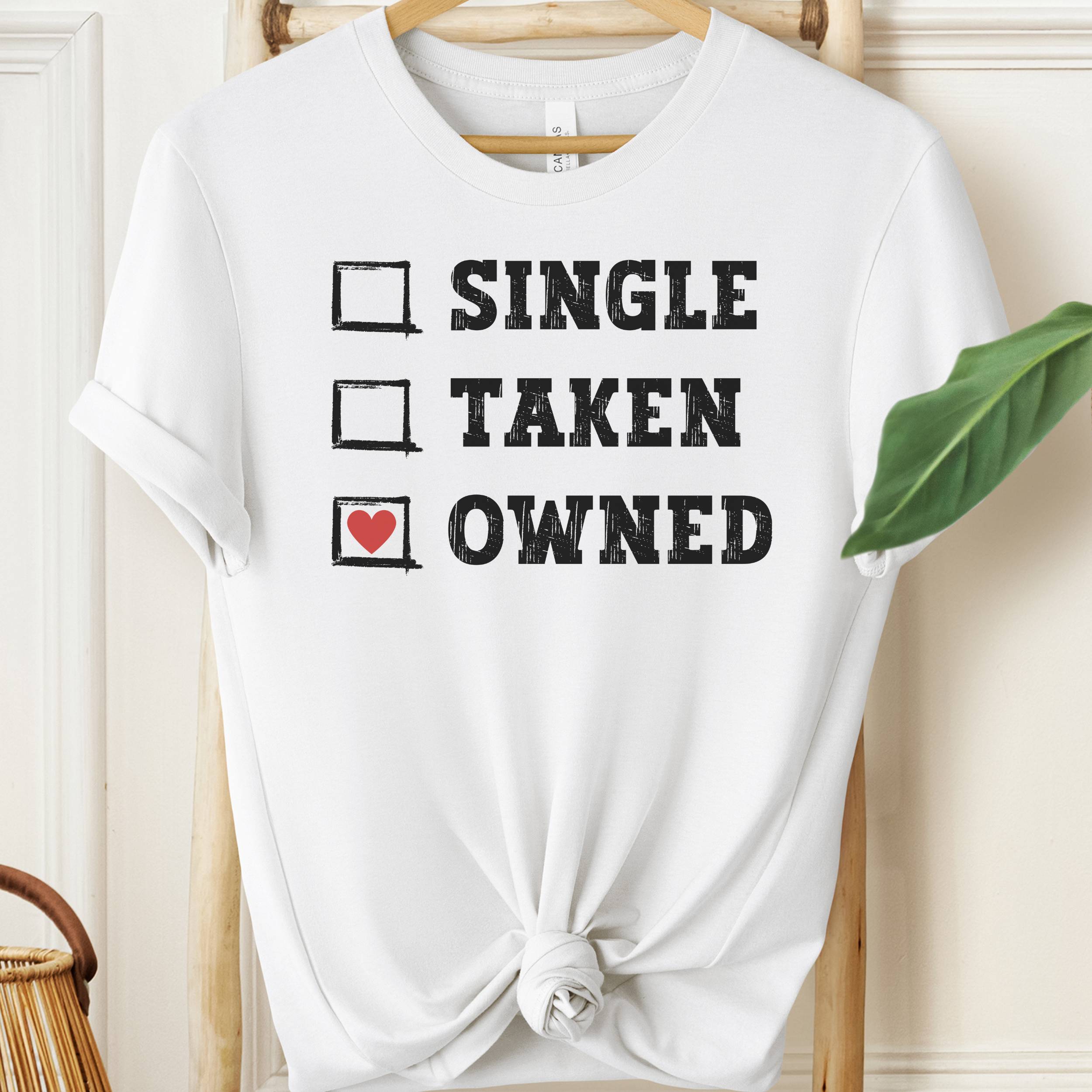 White t-shirt with text 'Single, Taken, Owned' on a hanger.