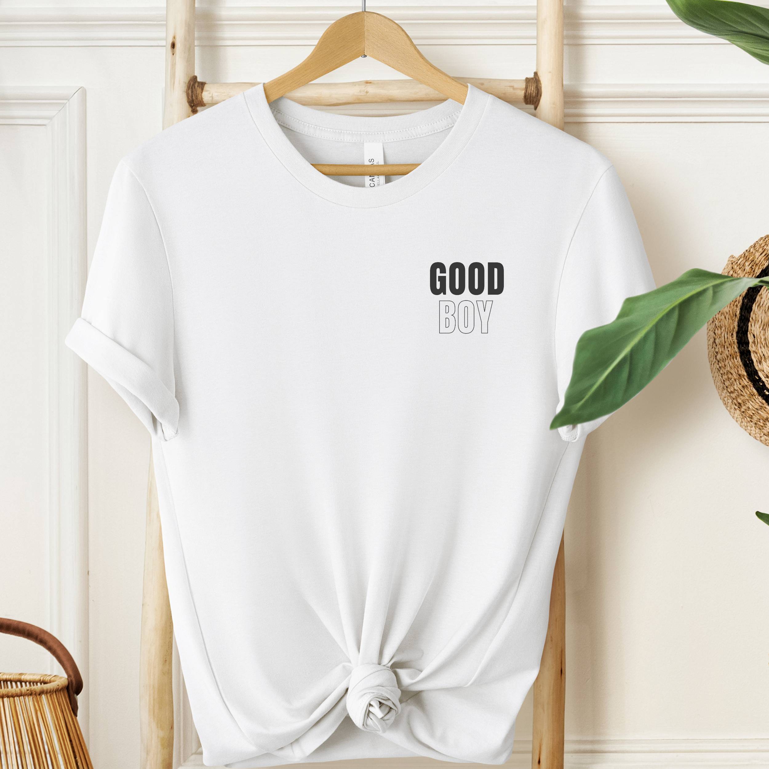 White t-shirt with 'GOOD BOY' text on a hanger against a neutral background