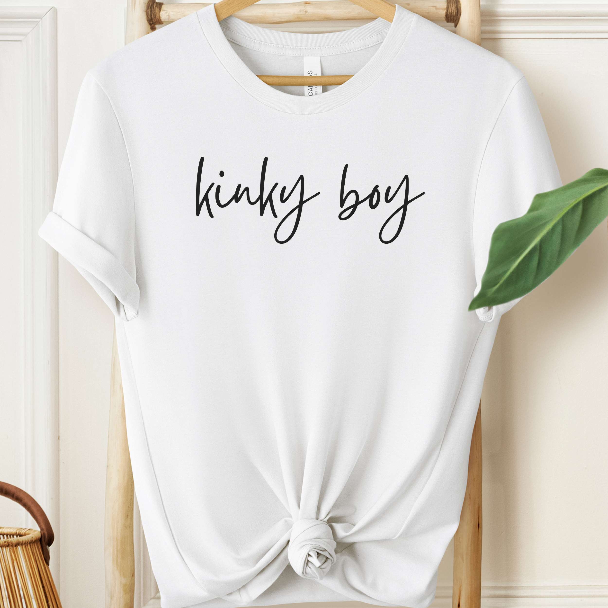 White t-shirt with 'kinky boy' text on a hanger against a neutral background