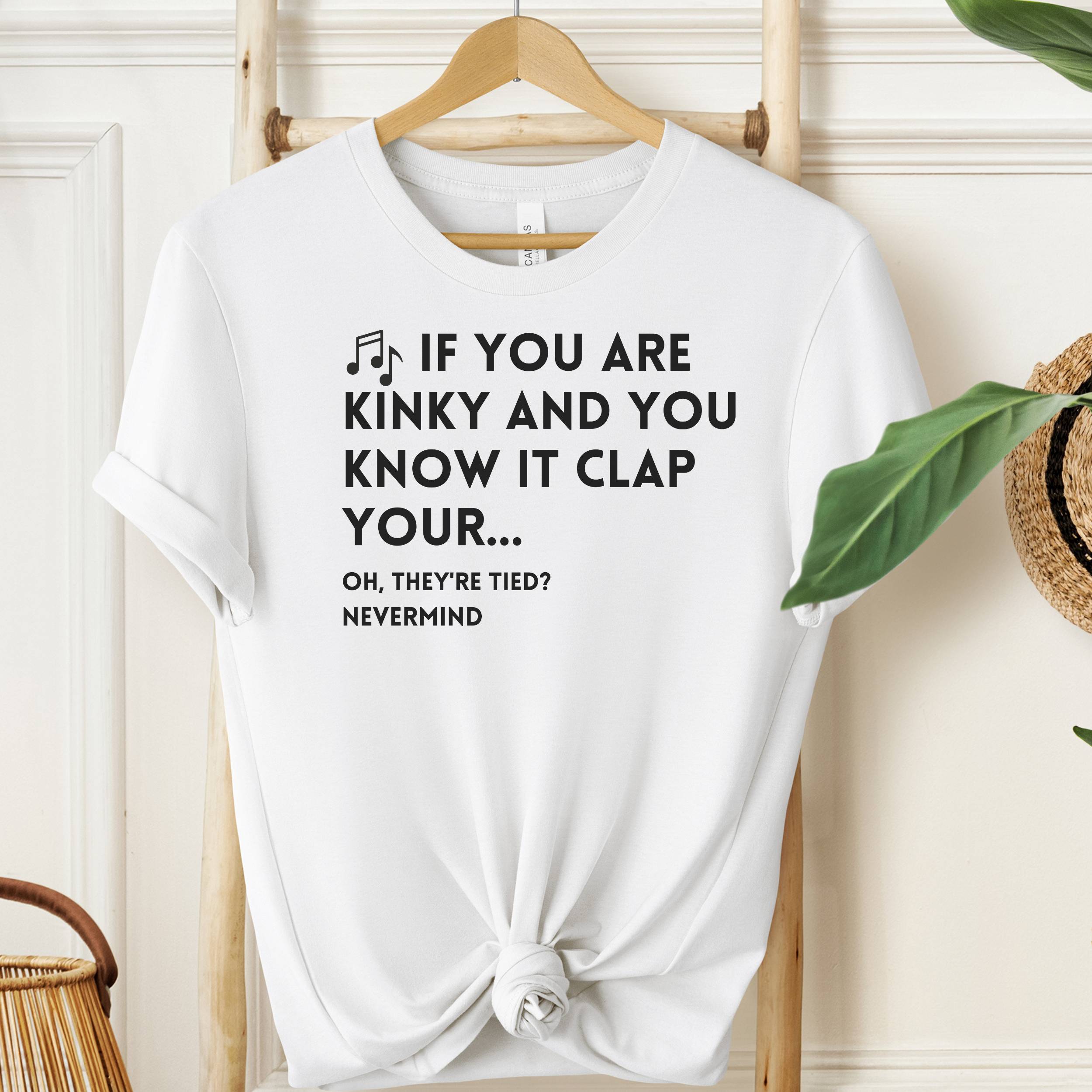 White t-shirt with humorous text design on a wooden hanger against a neutral background.