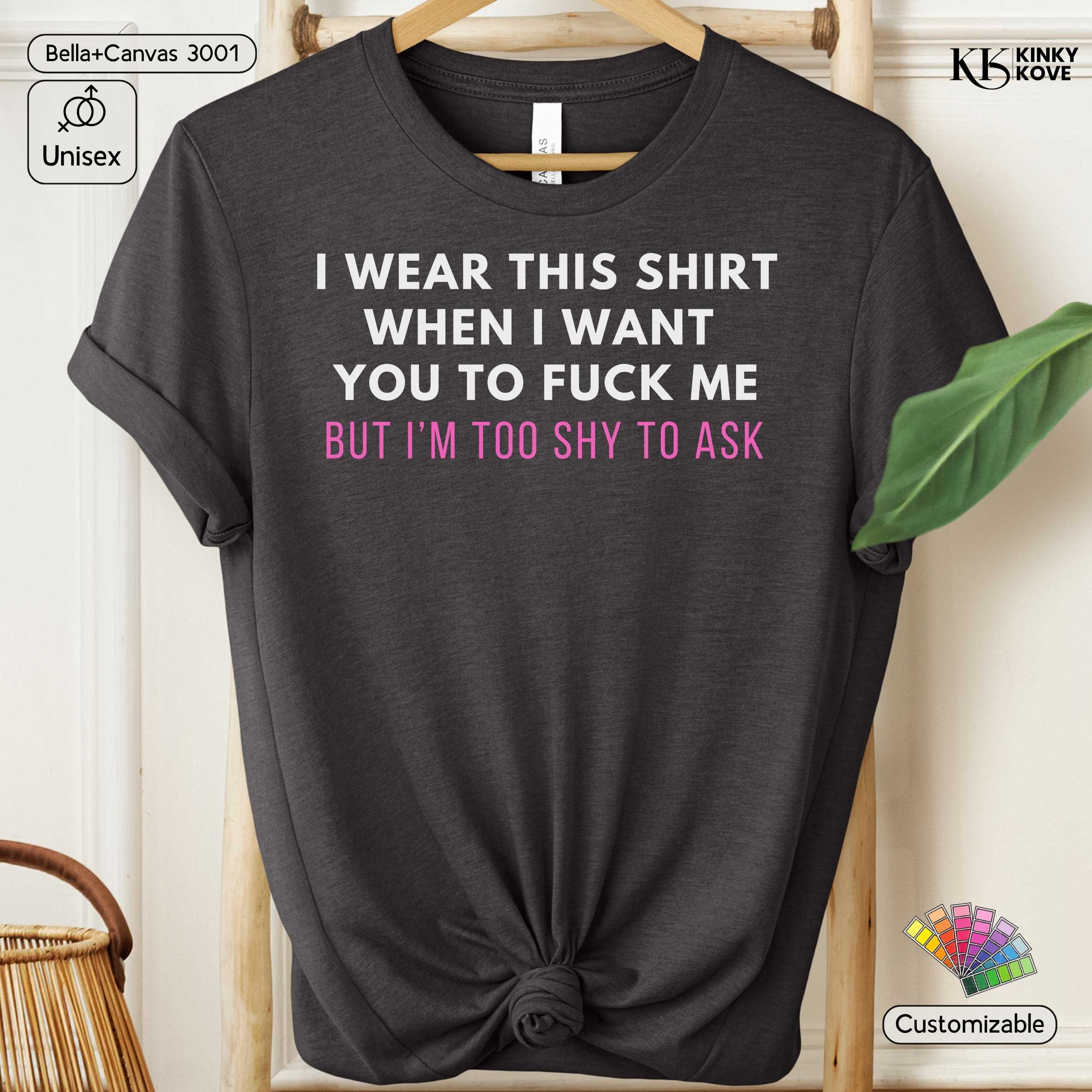 Black t-shirt with printed text on a hanger against a white wall.