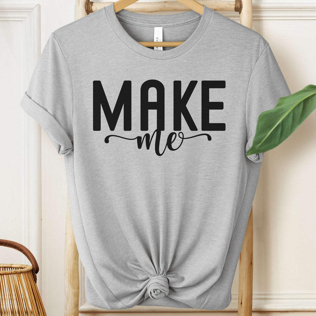 Gray t-shirt with 'MAKE me' text on a wooden hanger.
