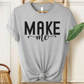 Gray t-shirt with 'MAKE me' text on a wooden hanger.