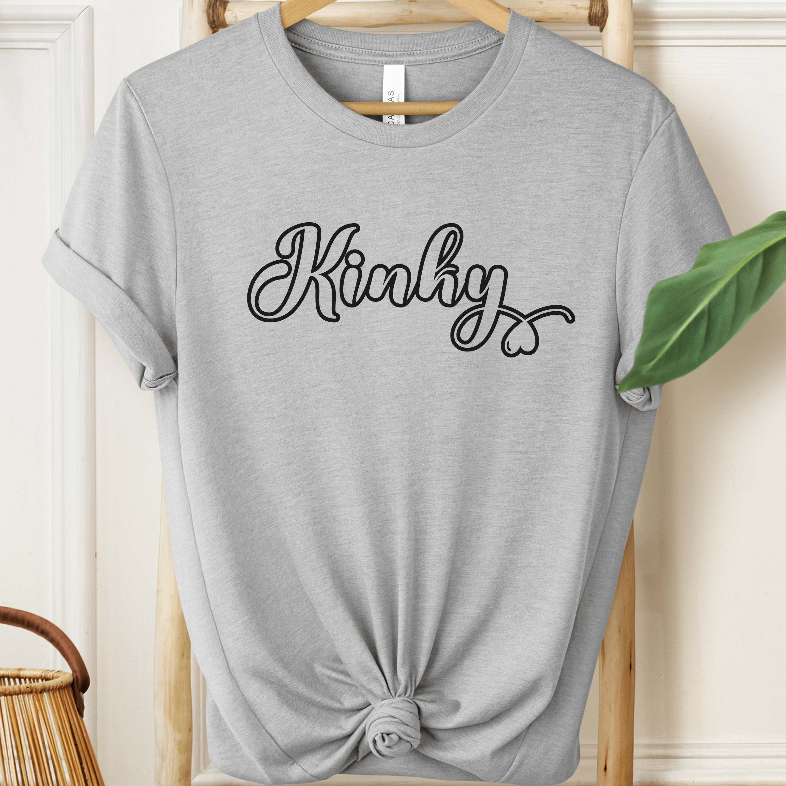 Gray t-shirt with 'Kinky' text on a hanger against a neutral background
