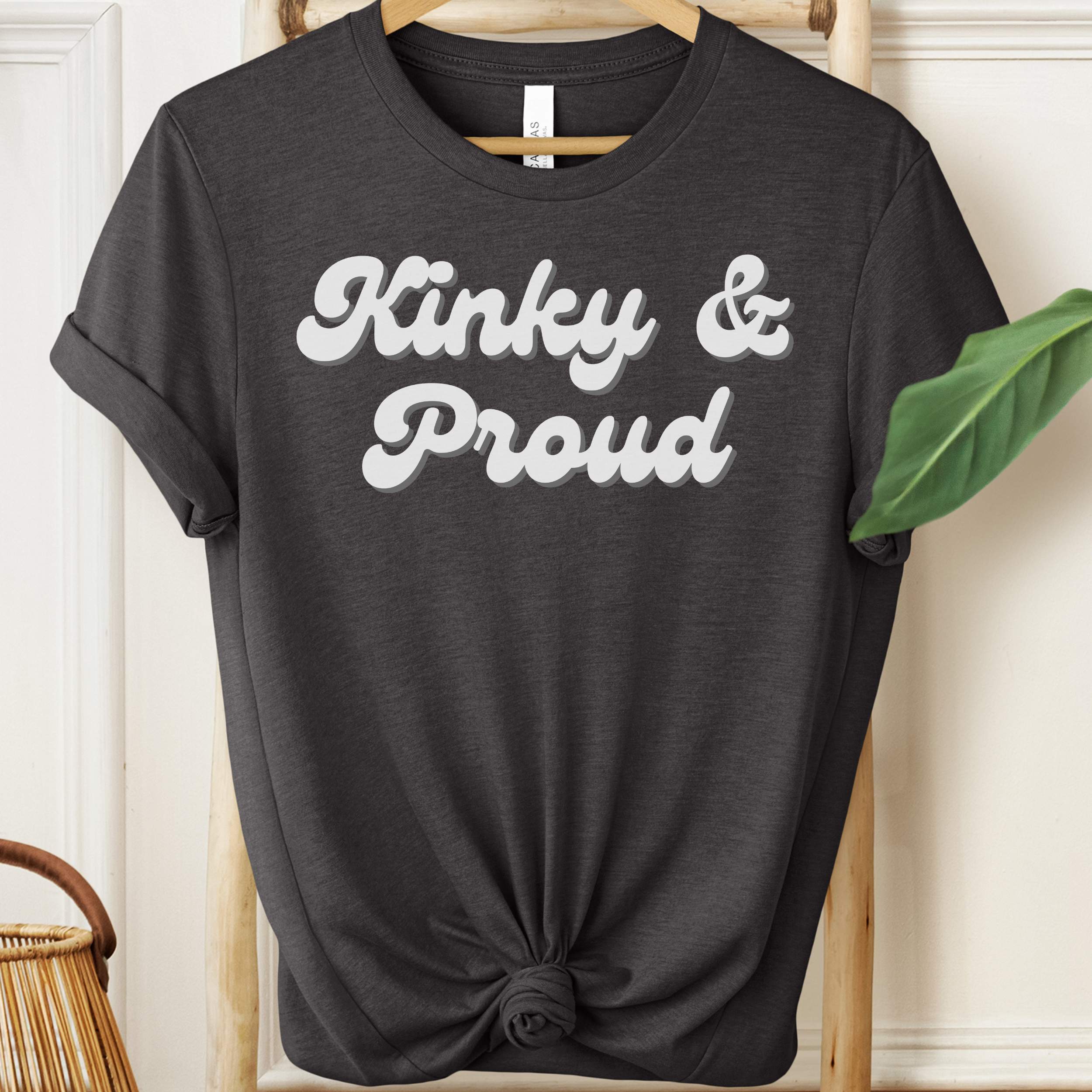 Black t-shirt with 'Kinky & Proud' text on a hanger against a neutral background