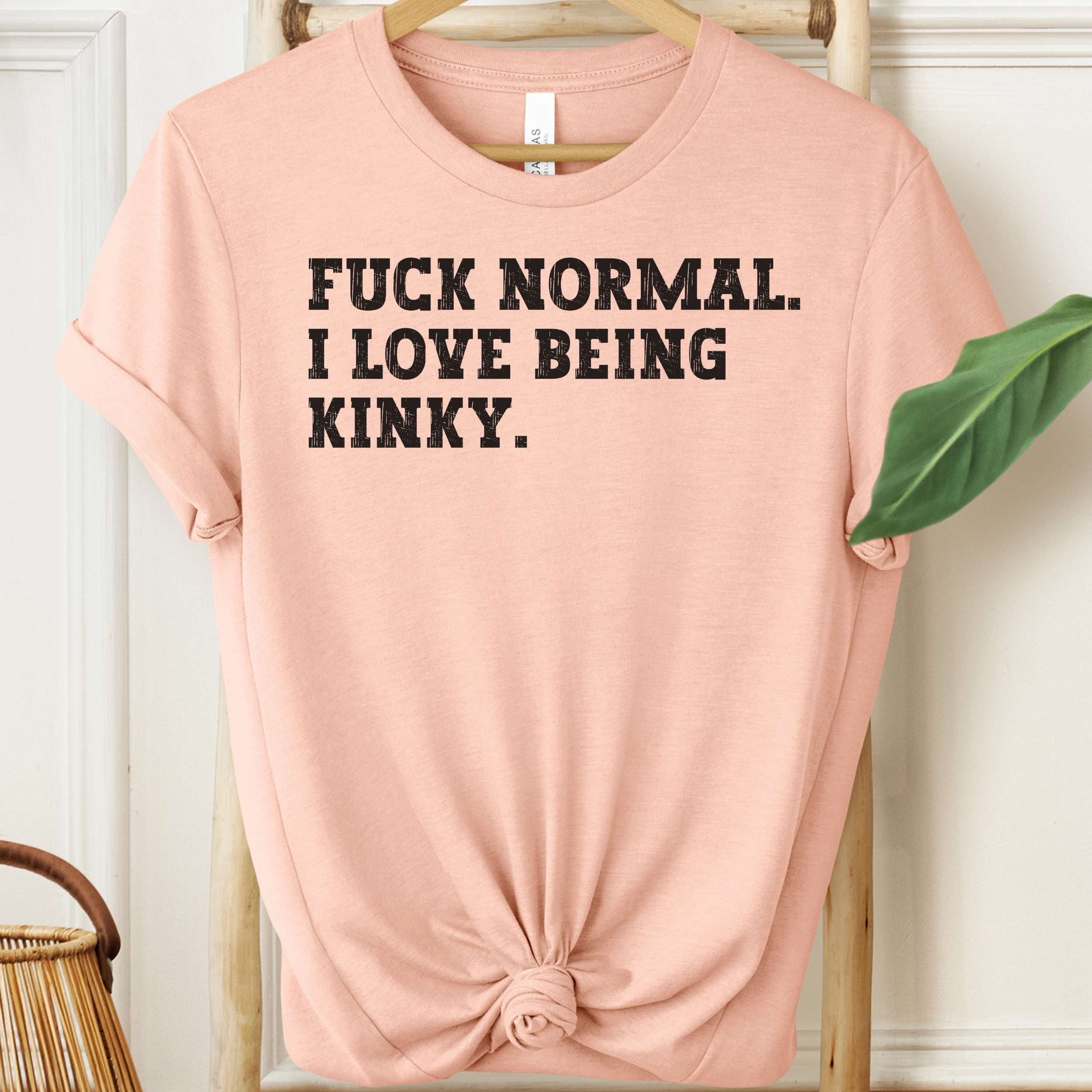 Pink t-shirt with black text on a hanger against a white wall.