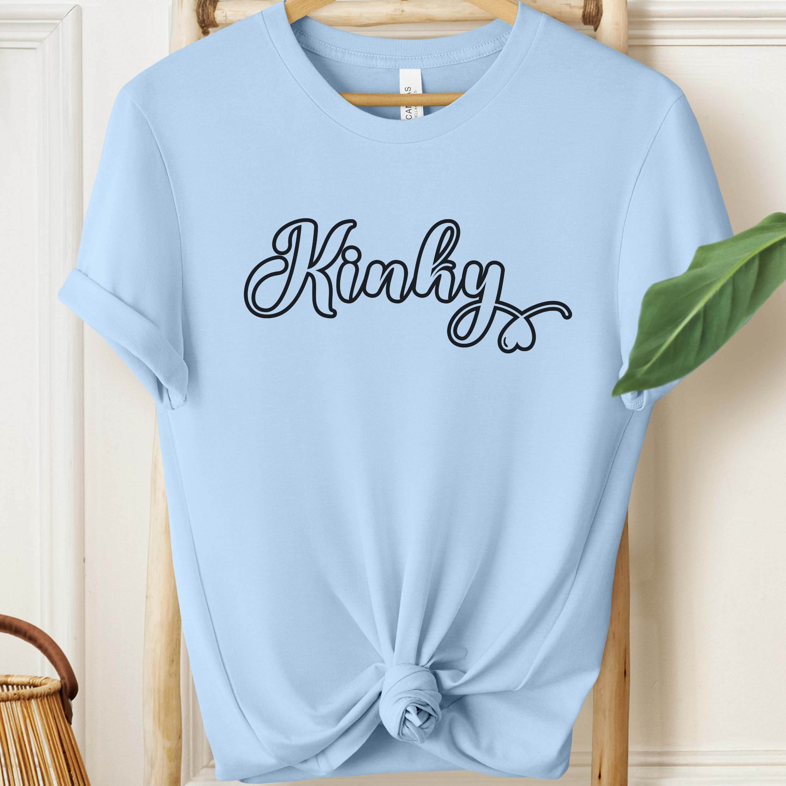 Light blue t-shirt with 'Kinky' text on a wooden hanger.
