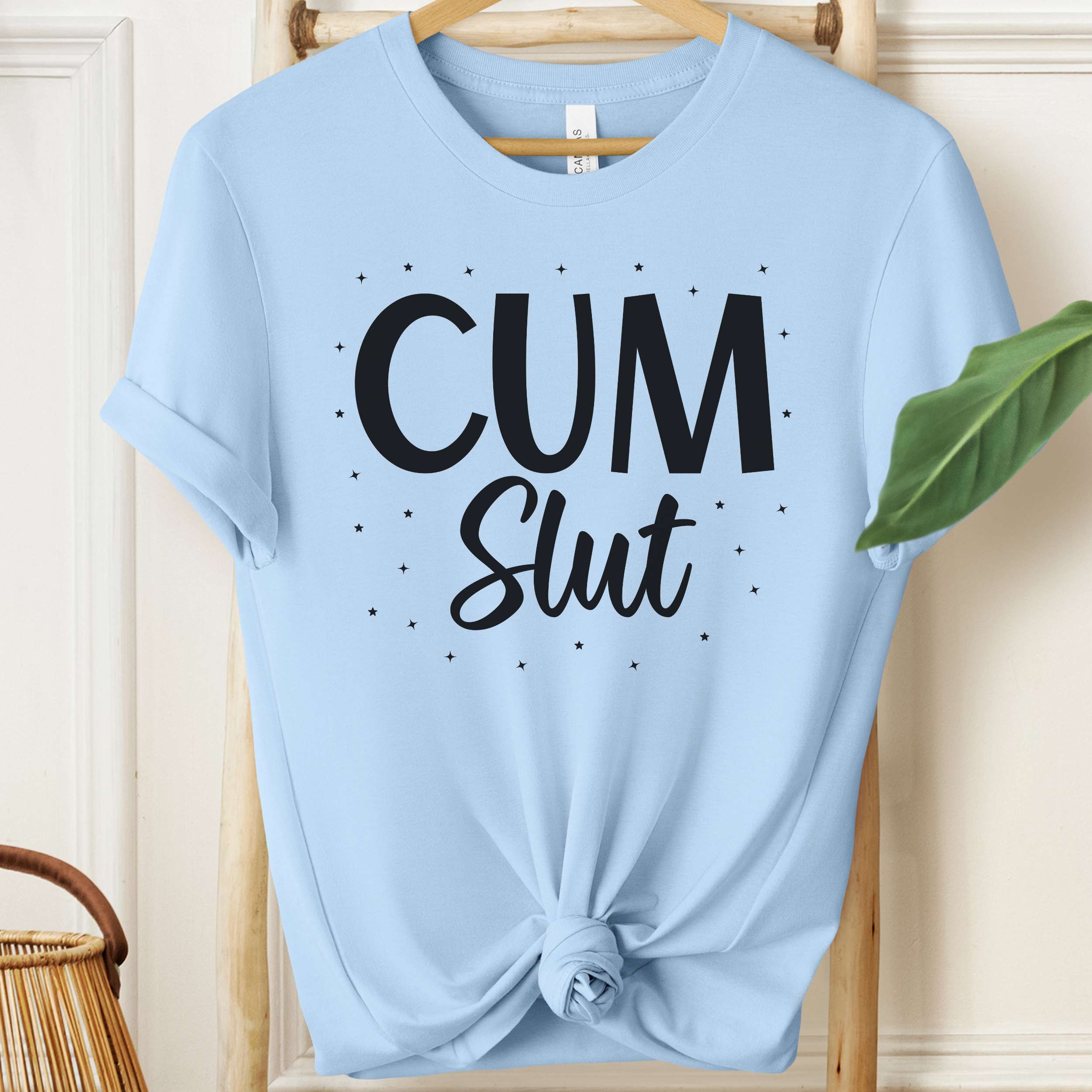 Light blue t-shirt with 'Cum Slut' text on a wooden hanger.