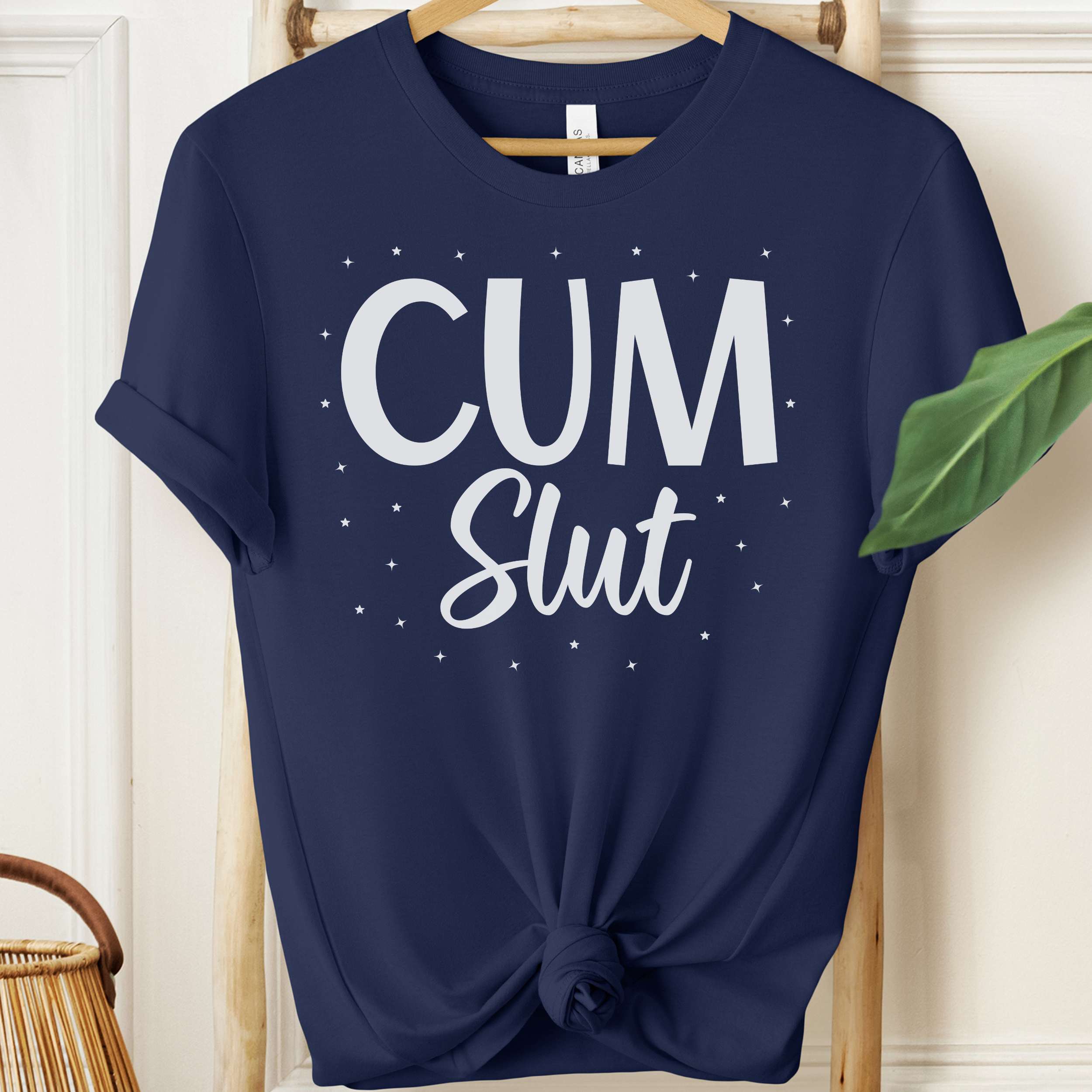 Navy blue t-shirt with 'Cum Slut' text on a hanger against a white wall.