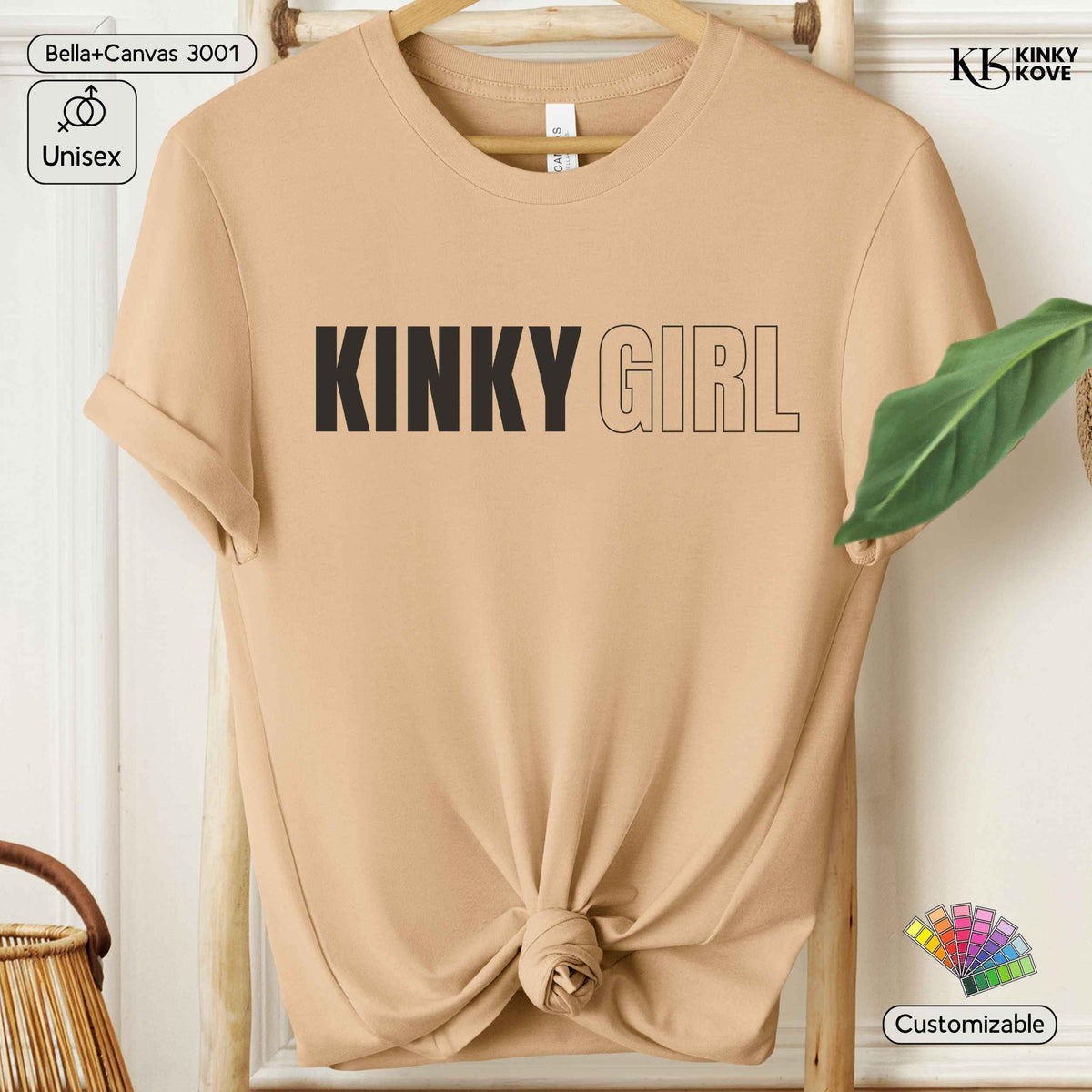 A beige short-sleeve t-shirt with 'KINKY GIRL' printed across the chest, styled on a wooden hanger with a knot at the bottom hem. The shirt features a color temperature scale graphic on the right side of the chest.