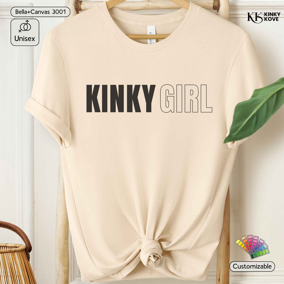 A beige short-sleeve t-shirt with 'KINKY GIRL' printed across the chest, styled on a wooden hanger with a knot at the bottom hem. The text 'KINKY GIRL' is in black, while 'GIRL' is outlined.