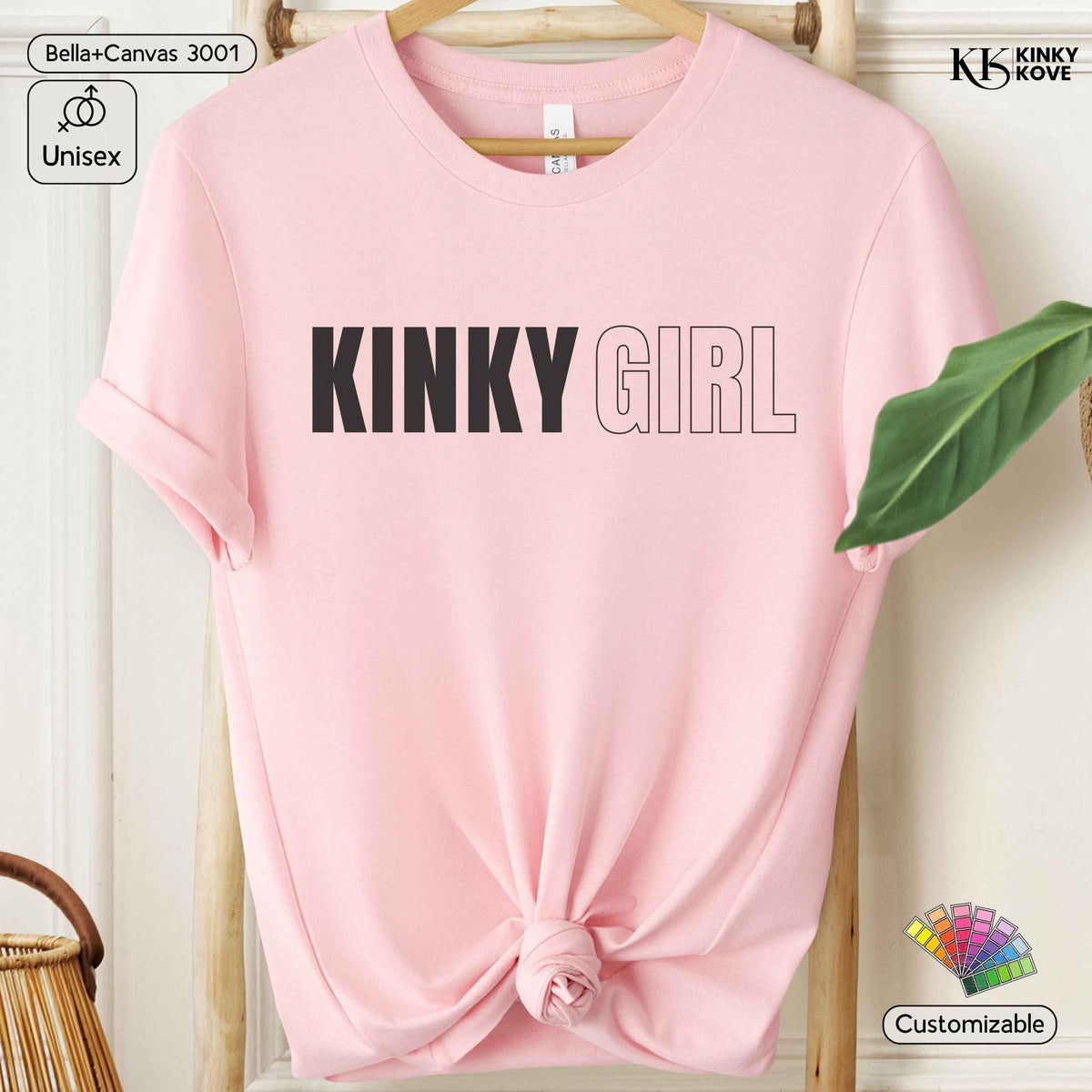 A light pink short-sleeve t-shirt with 'KINKY GIRL' printed across the chest, styled on a wooden hanger with a knot at the bottom hem. The image includes decorative elements like a green leaf, a wicker basket, and text badges indicating 'Bella+Canvas 3001', 'Unisex', 'KINKY KOVE', and 'Customizable'.