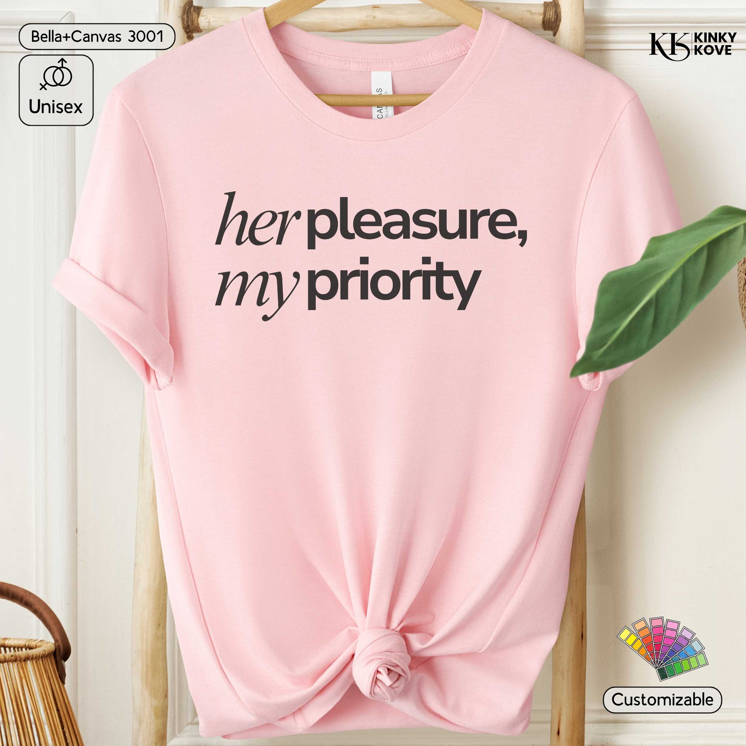 Pink t-shirt with 'her pleasure, my priority' text on a hanger with branding visible.