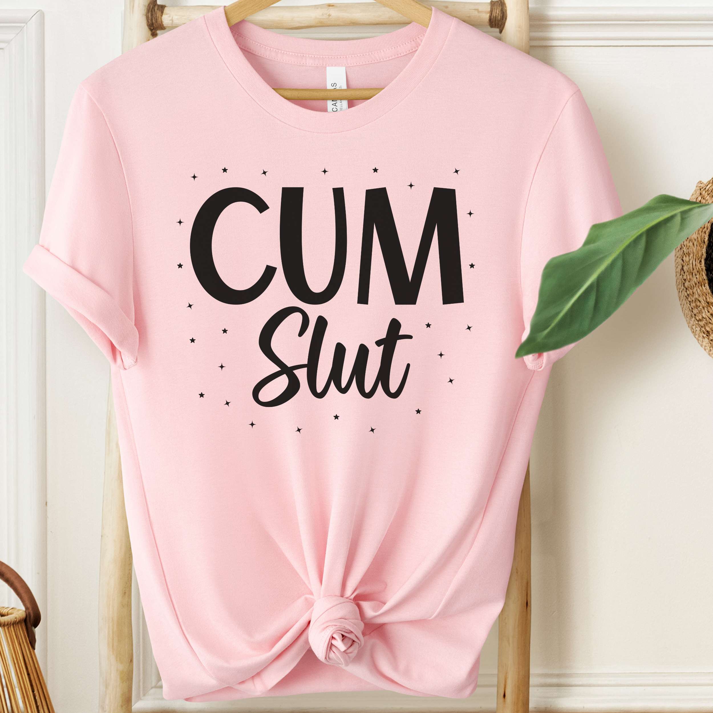 Pink t-shirt with 'Cum Slut' text on a wooden hanger.