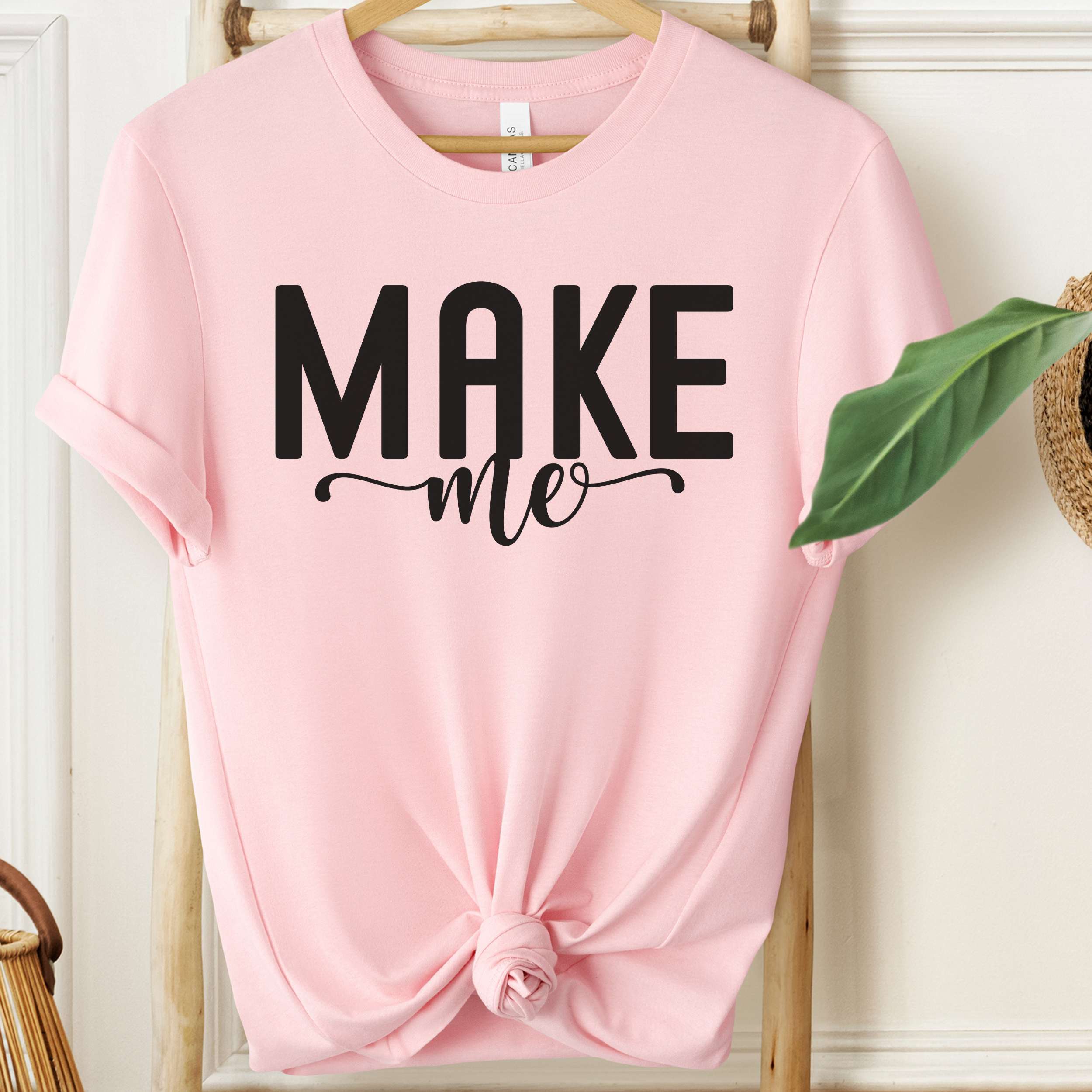 Pink t-shirt with 'MAKE me' text on a wooden hanger.