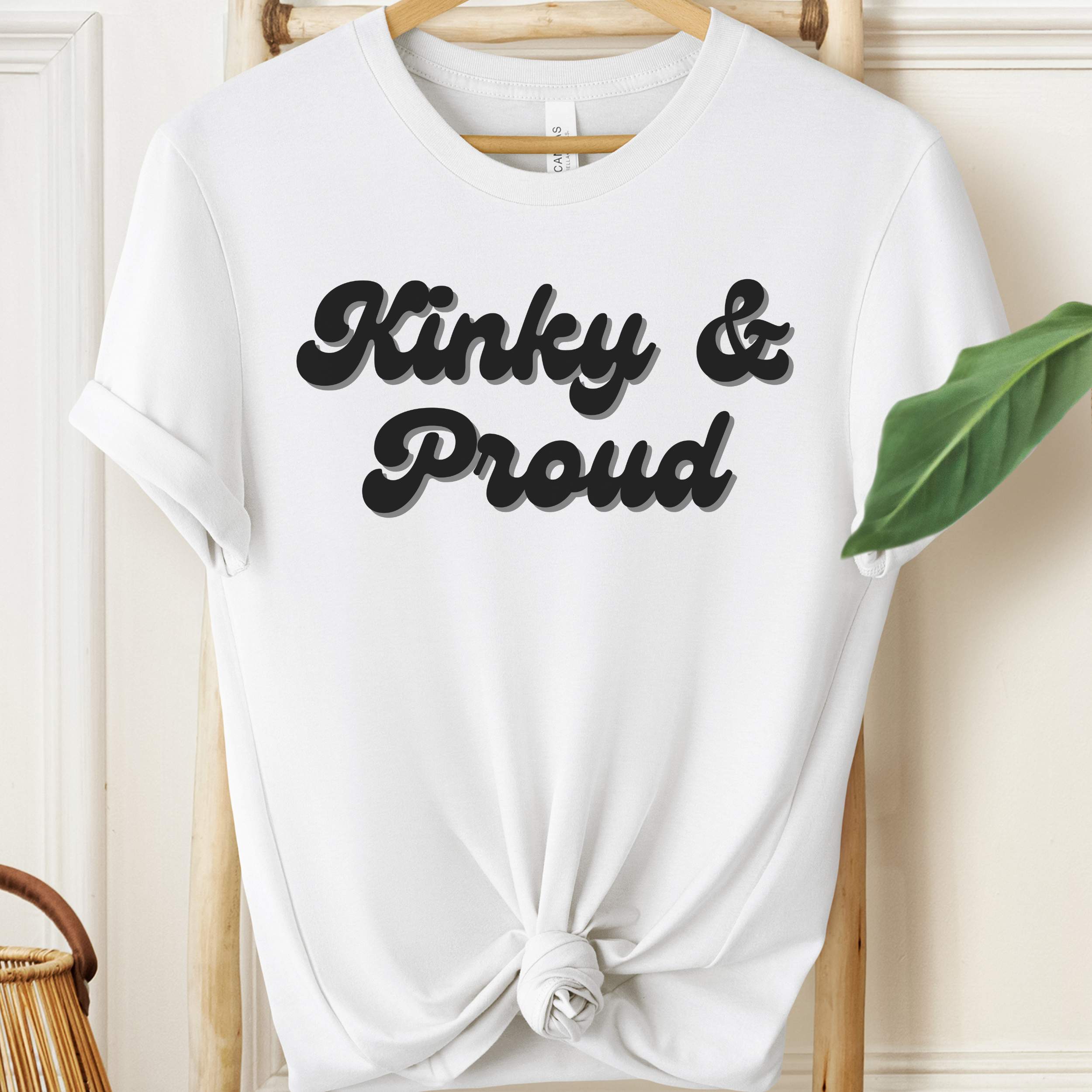 White t-shirt with 'Kinky & Proud' text on a hanger against a neutral background