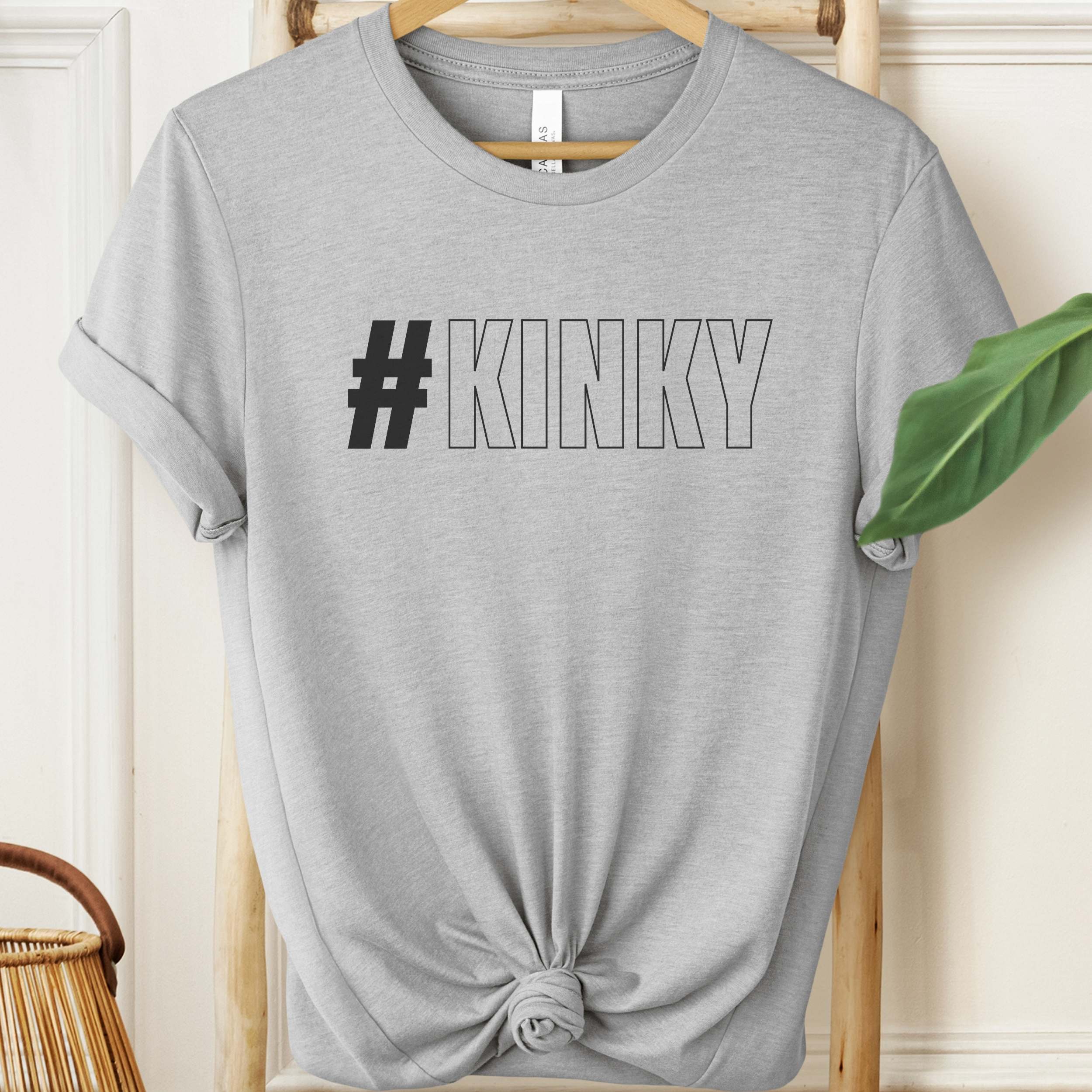 Gray t-shirt with '#KINKY' text on a hanger against a neutral background