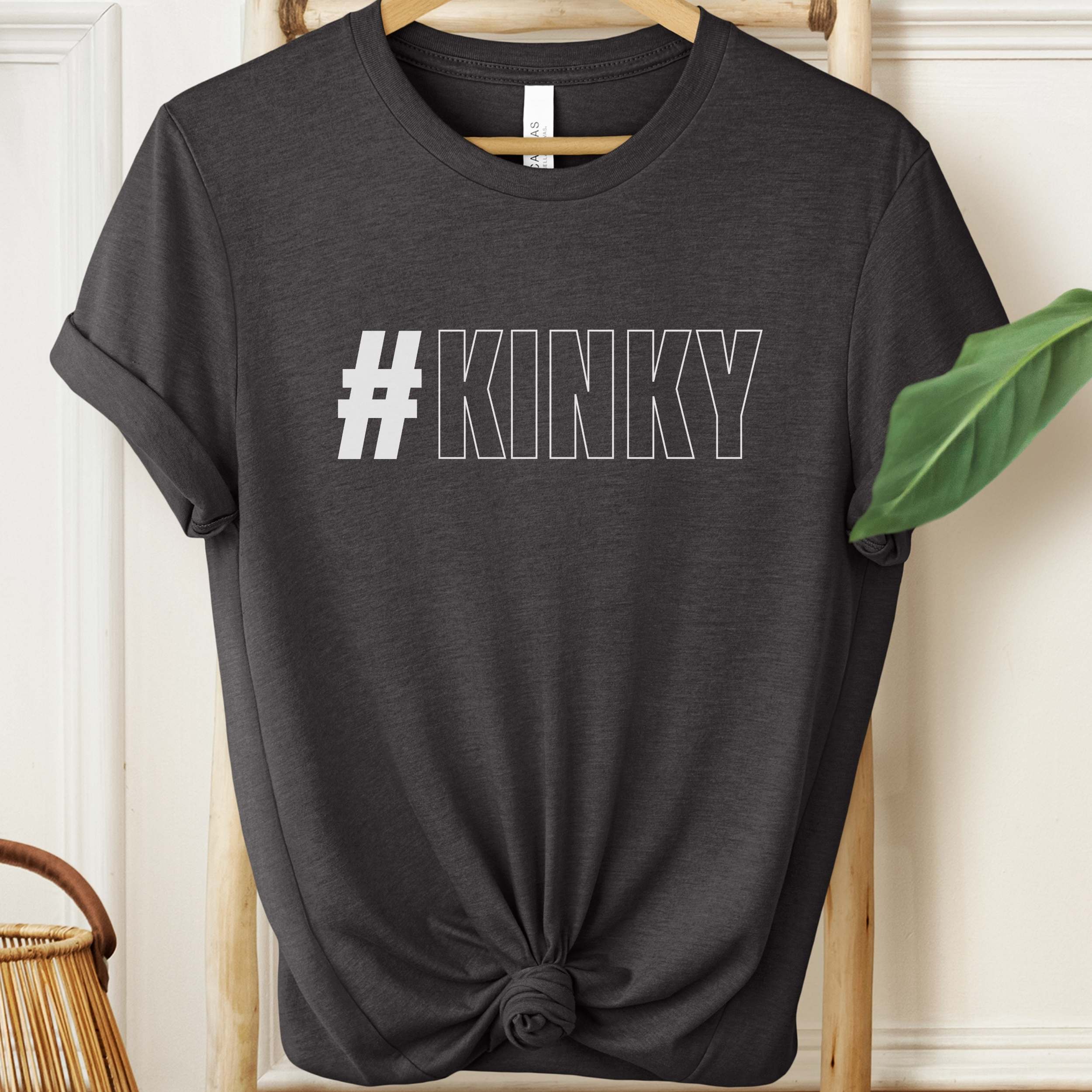 Black t-shirt with '#KINKY' text on a hanger against a neutral background