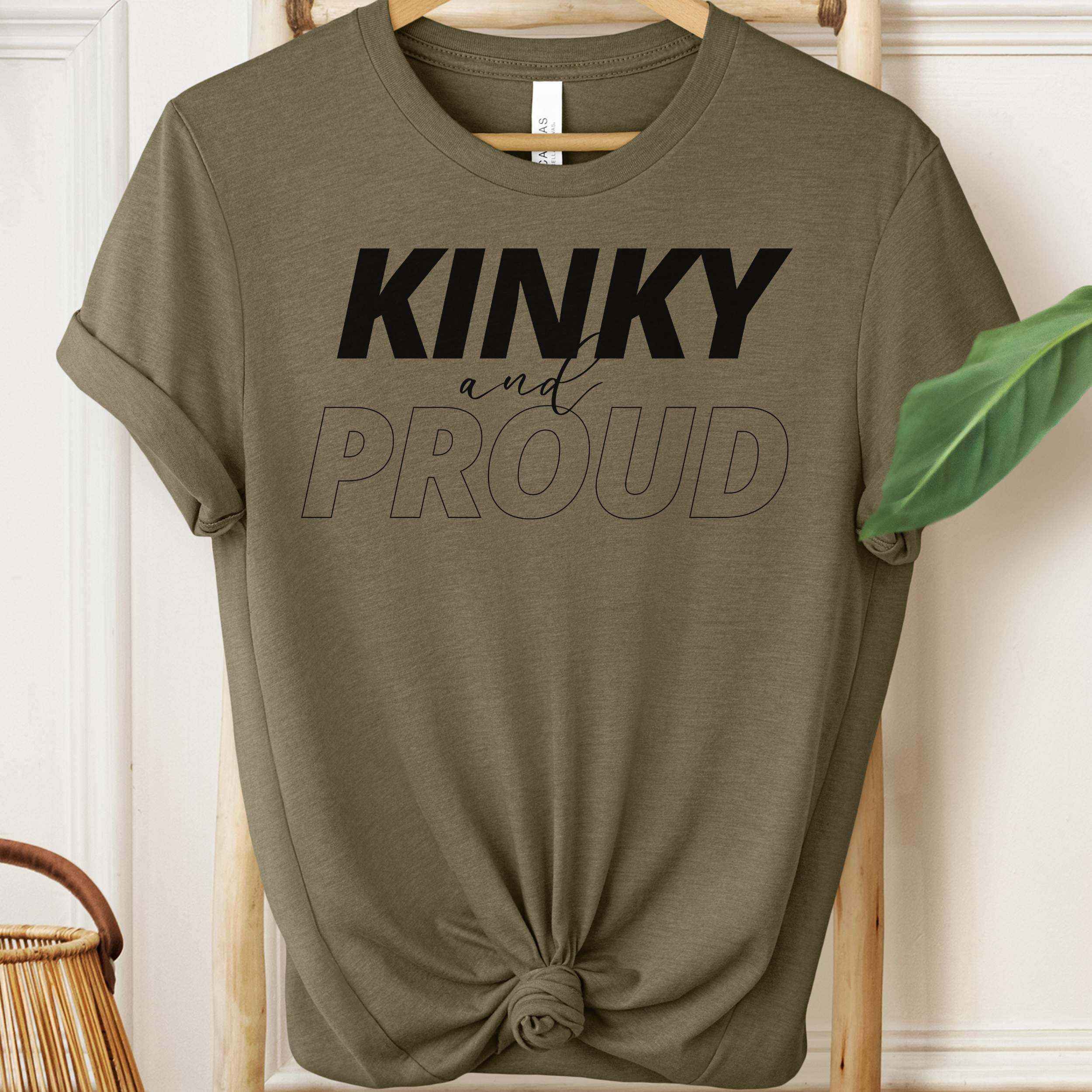 Olive green t-shirt with 'Kinky and Proud' text on a hanger.