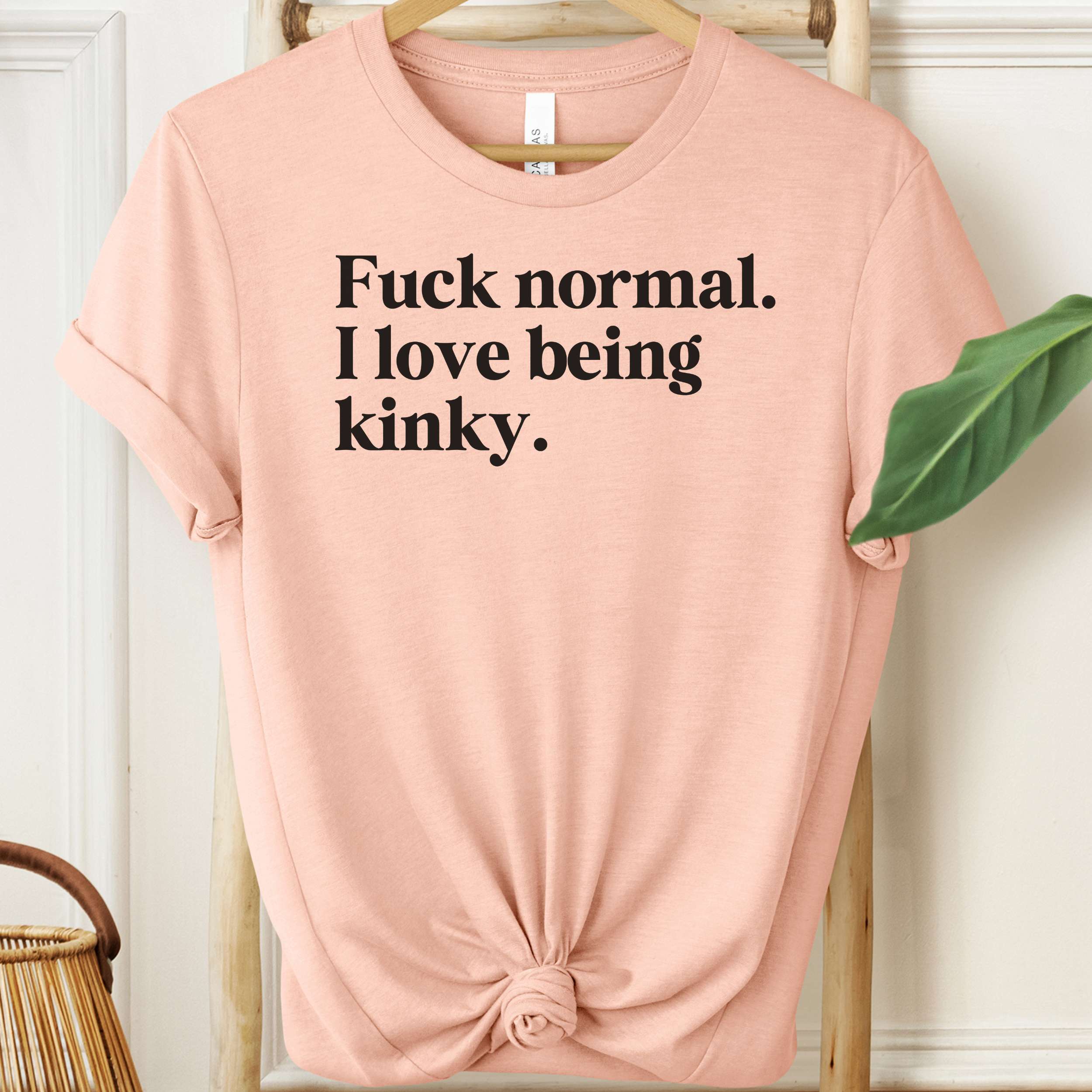 Pink t-shirt with black text on a hanger against a white wall.