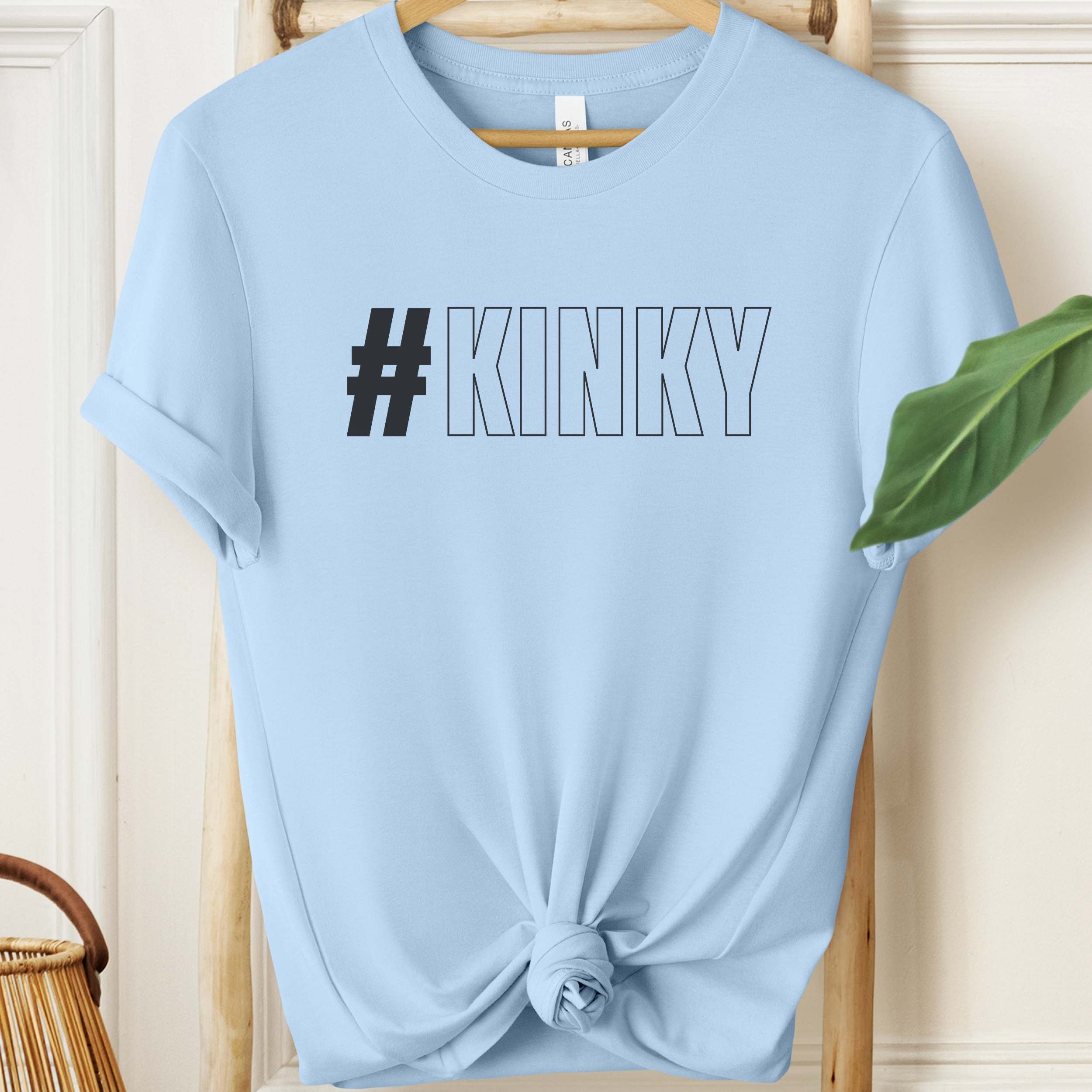 Light blue t-shirt with '#KINKY' text on a wooden hanger.