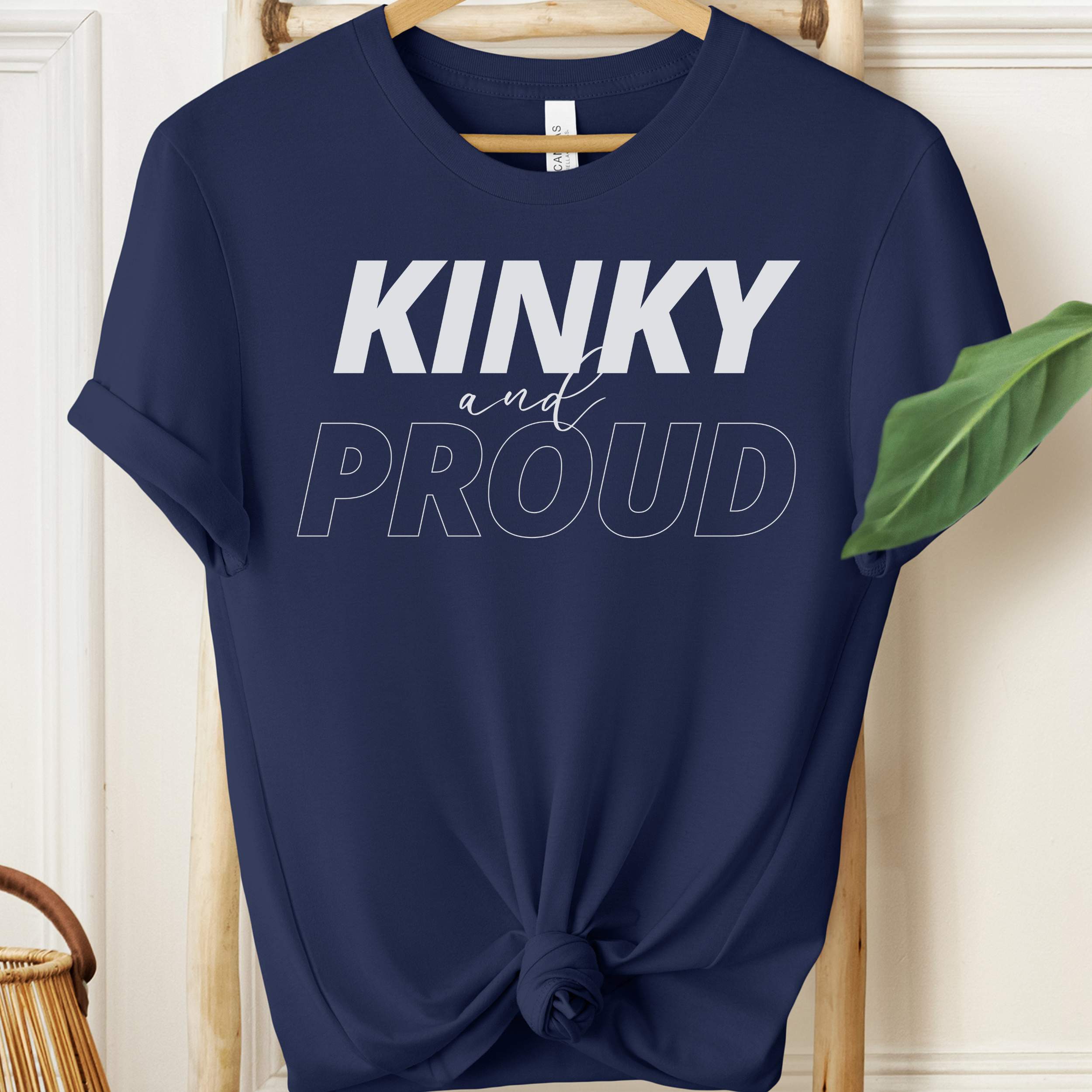 Navy blue t-shirt with 'Kinky and Proud' text on a wooden hanger.