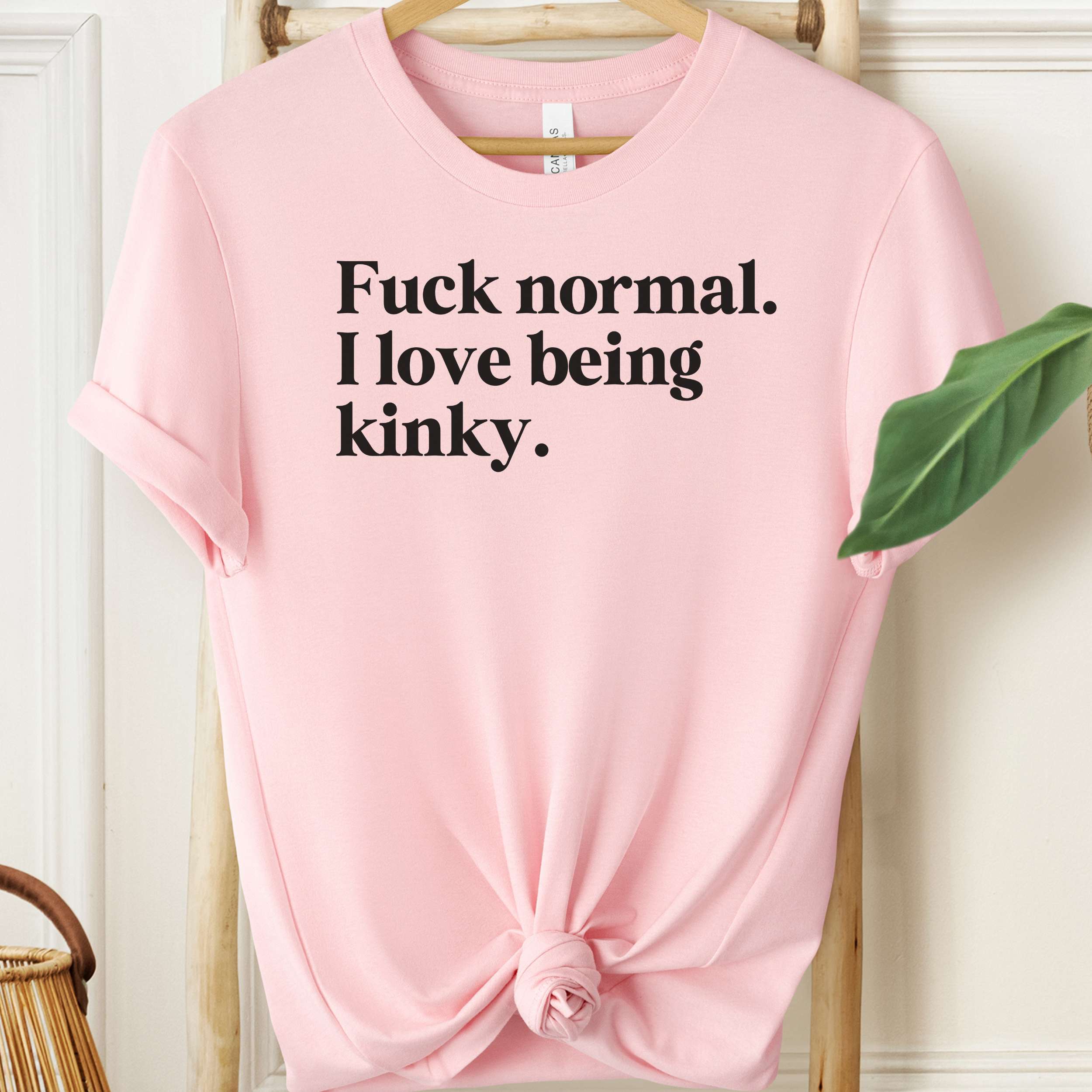 Pink t-shirt with black text on a hanger against a white wall.