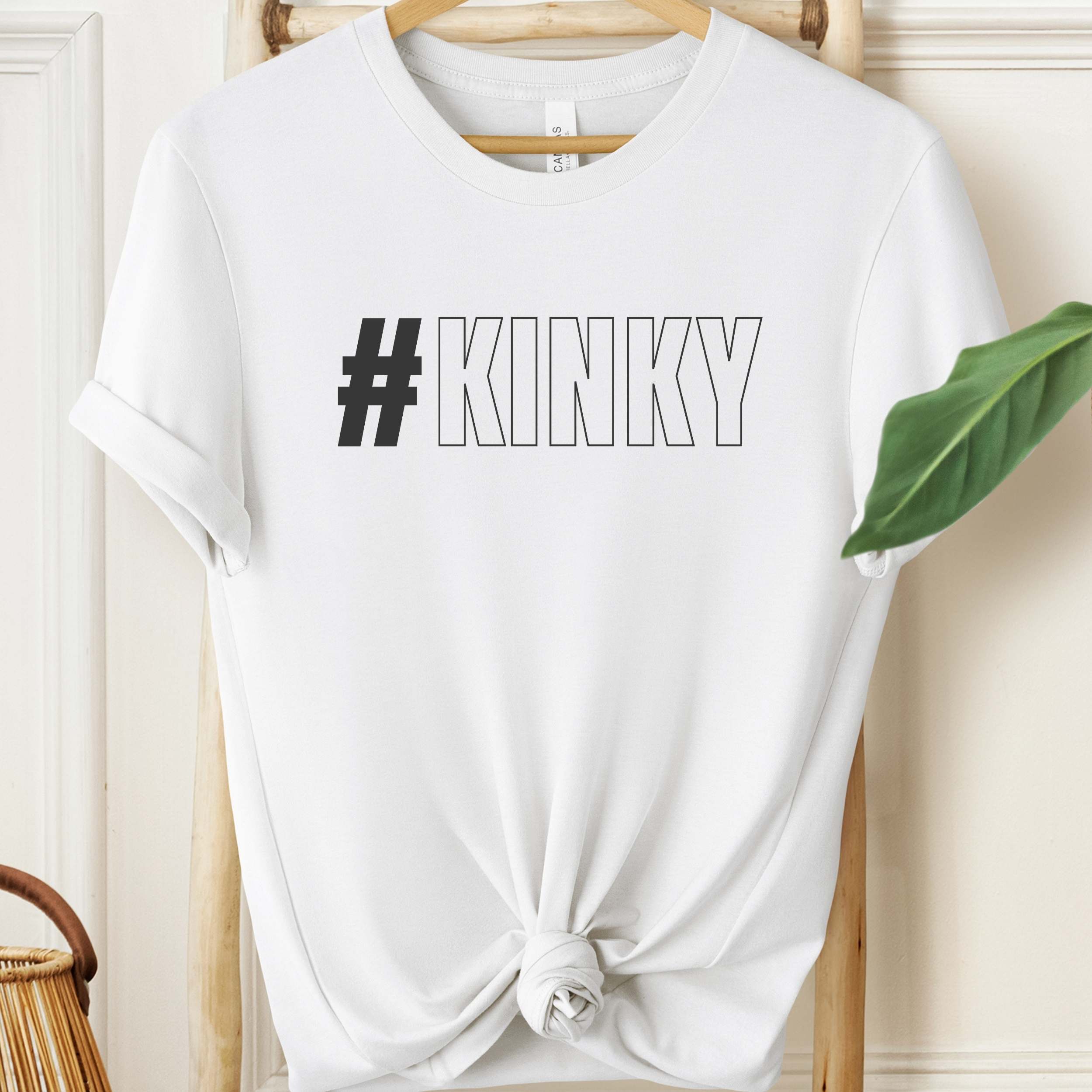 White t-shirt with '#KINKY' text on a hanger against a neutral background