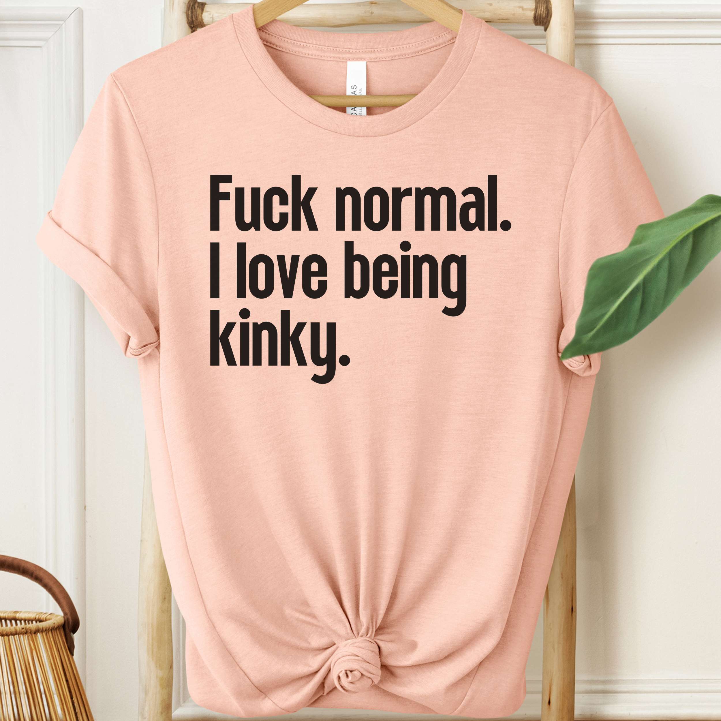 Pink t-shirt with black text on a hanger against a white wall.