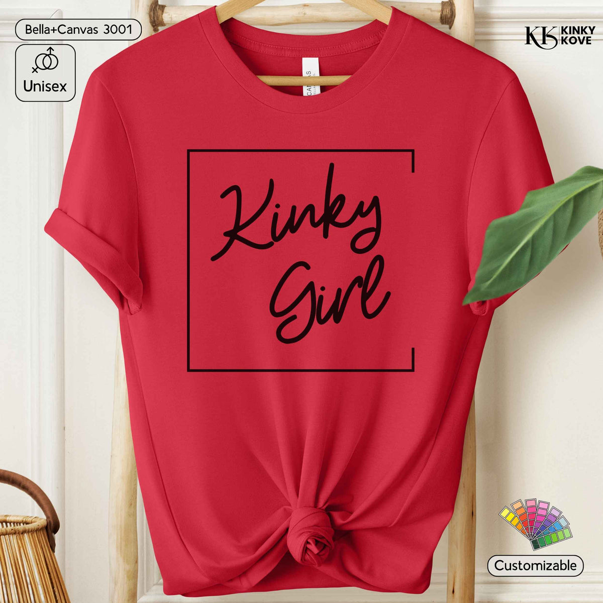 A red short-sleeve t-shirt hanging on a wooden hanger, styled with a knot at the bottom hem. The shirt features a black graphic print that reads 'Kinky Girl' inside a thin black rectangular border.