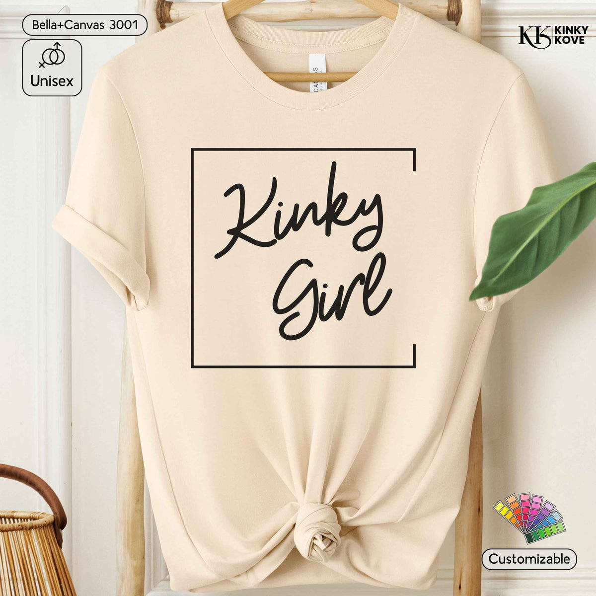 A beige short-sleeve t-shirt on a wooden hanger, styled with a knot at the bottom hem. The shirt features a black graphic print that reads 'Kinky Girl' inside a thin square border.