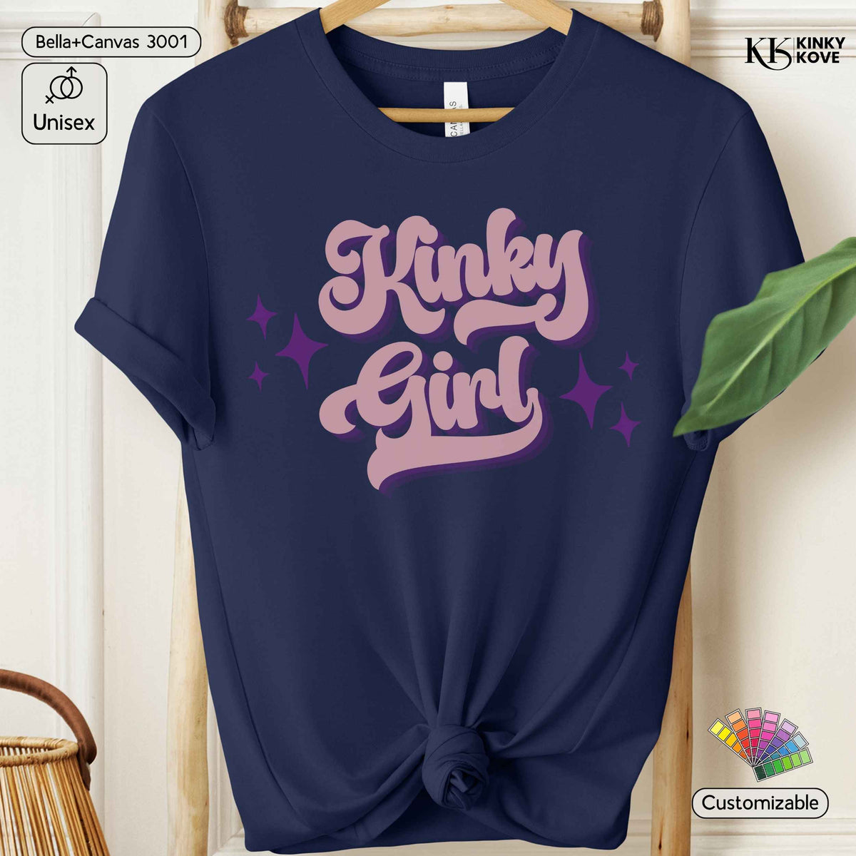 A navy blue short-sleeve t-shirt hanging on a wooden hanger, styled with a knot at the bottom hem. The shirt features a graphic print on the front reading 'Kinky Girl' in a pink bubble font with a purple shadow and purple star accents.