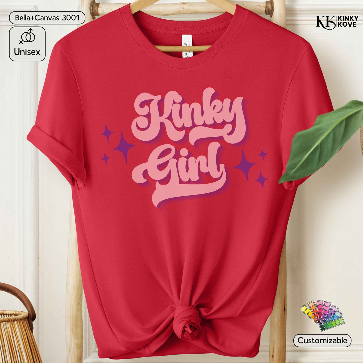 A red short-sleeve t-shirt on a wooden hanger, styled with a knot at the bottom hem. The shirt features a retro-style pink graphic that reads 'Kinky Girl' with purple star accents.
