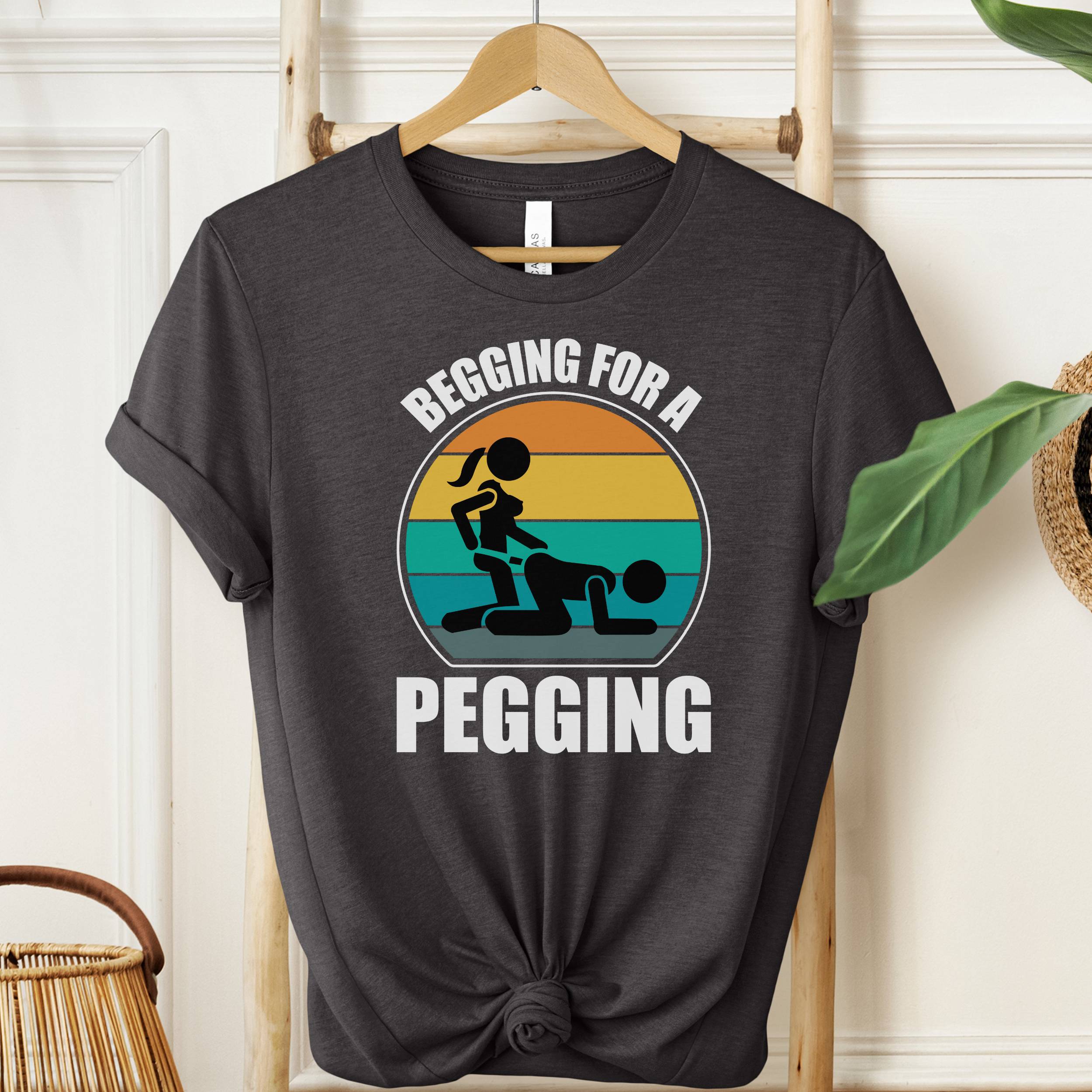 Black t-shirt with graphic design and text 'Begging for a Pegging' on a hanger.