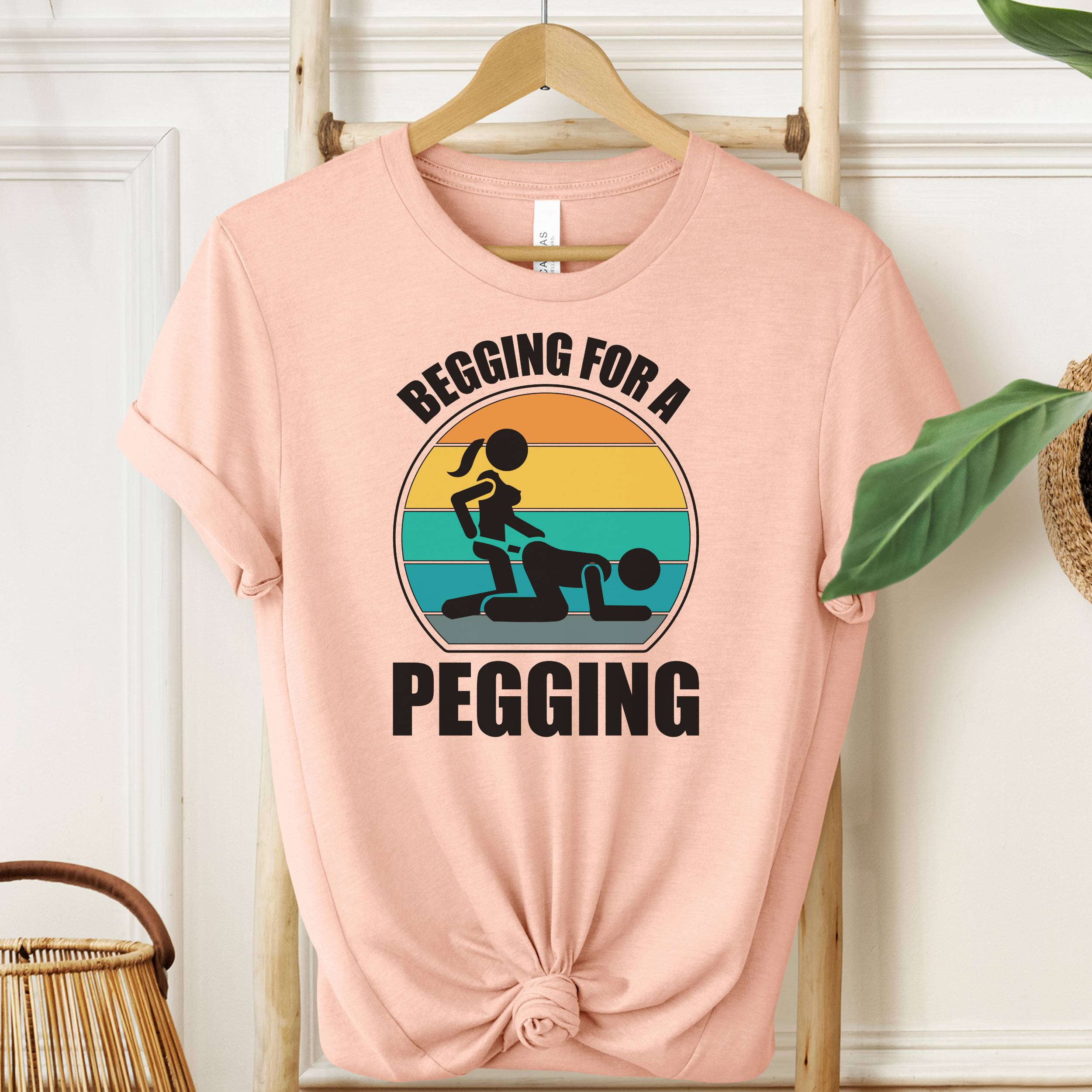 Pink t-shirt with graphic design and text on a hanger against a white wall.