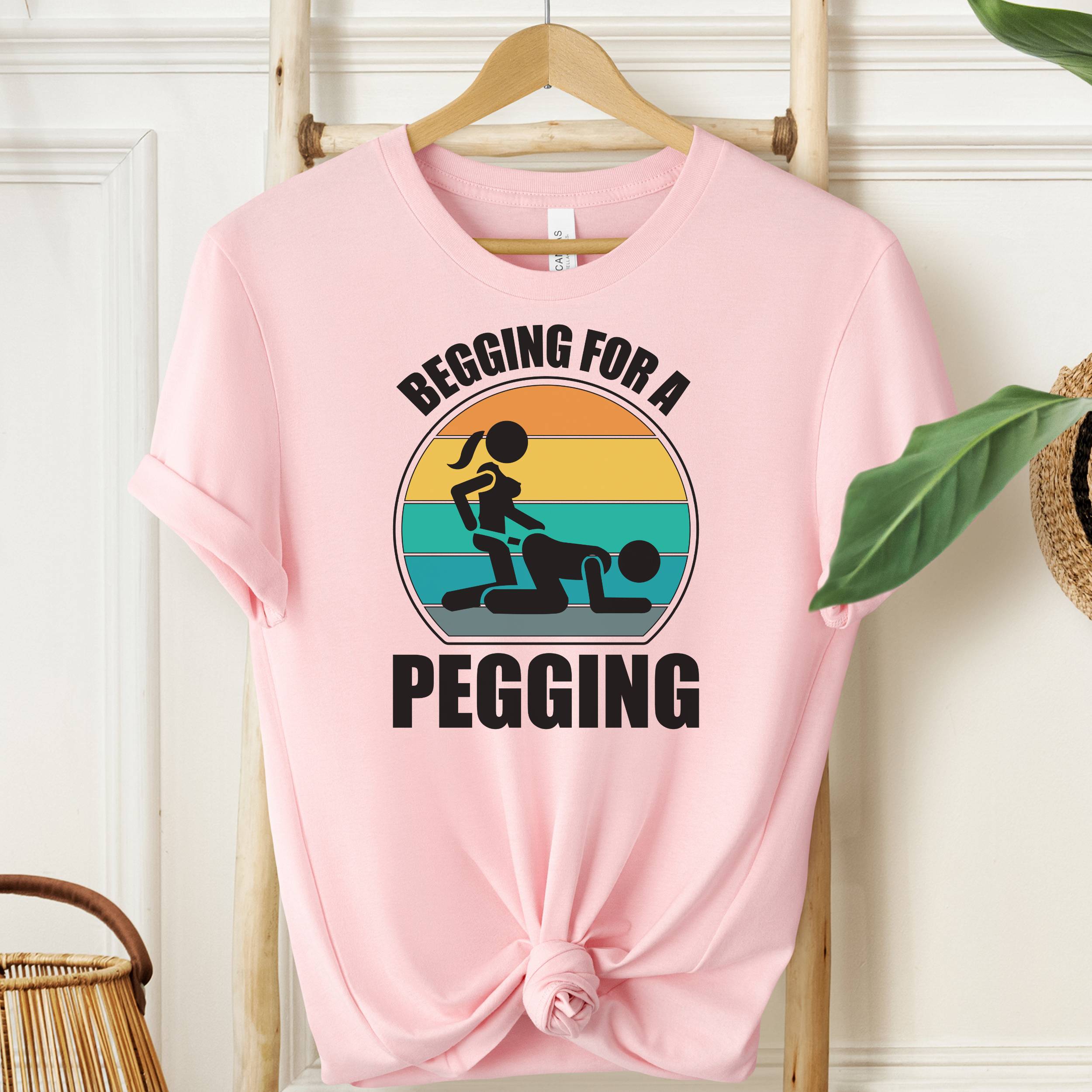 Pink t-shirt with graphic design and text on a hanger against a white wall.